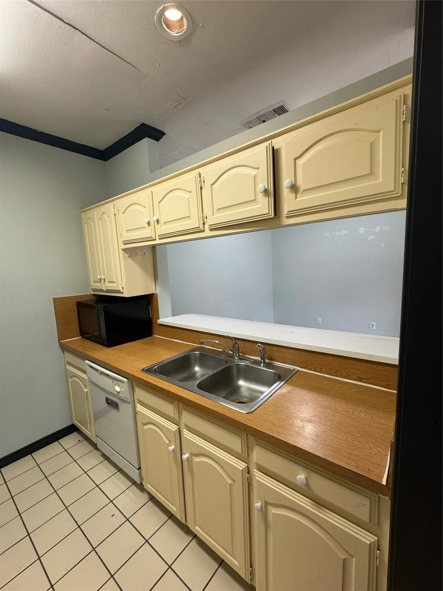 Kitchen area featuring a dual basin stainless steel sink, wood-finish countertops, light-colored cabinetry, a built-in dishwasher, and recessed ceiling lighting