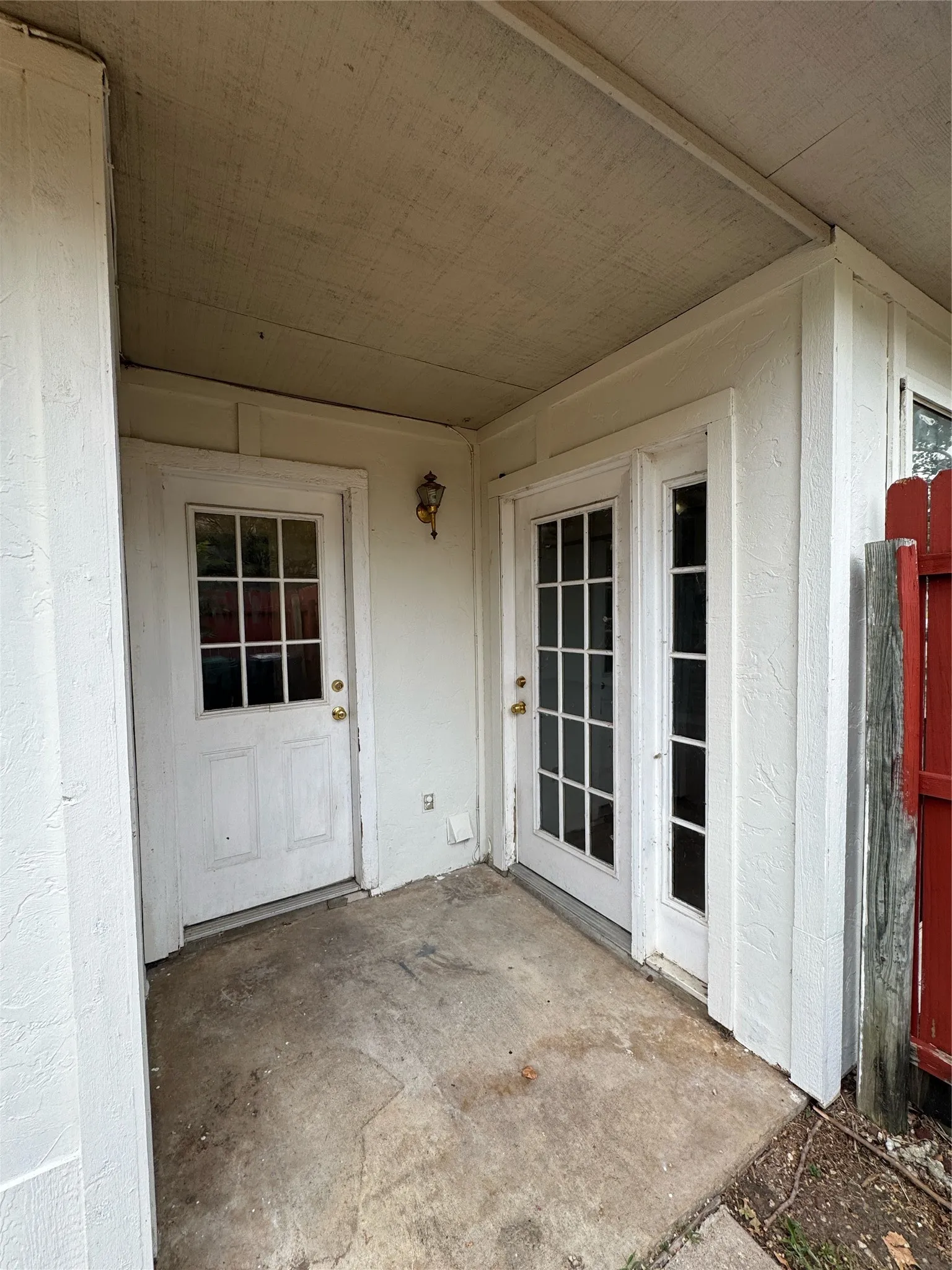 Covered exterior patio featuring a concrete surface, two white doors with glass panes, and an exterior wall light fixture