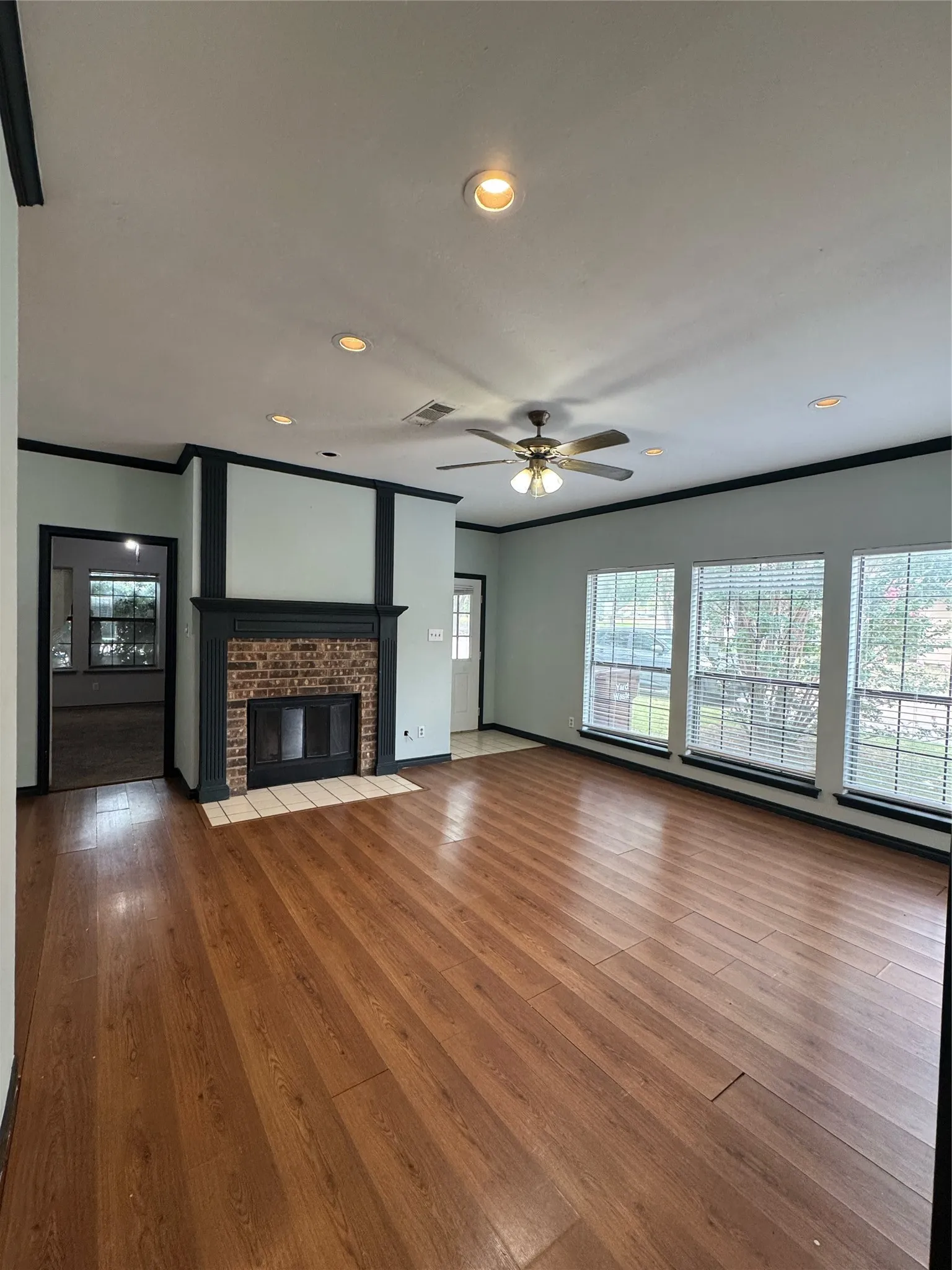 Expansive living space featuring wood-finish flooring, a brick fireplace with a dark wood mantle, and multiple windows