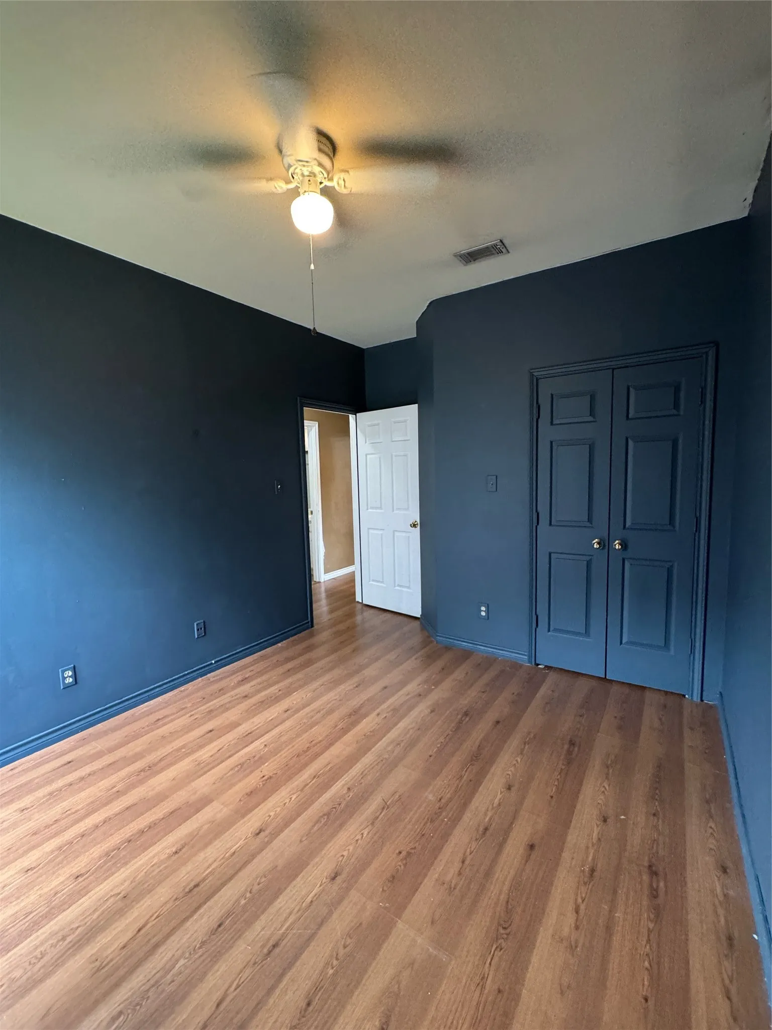 Room featuring wood-finish flooring, dark-toned walls, and a ceiling fan with integrated lighting