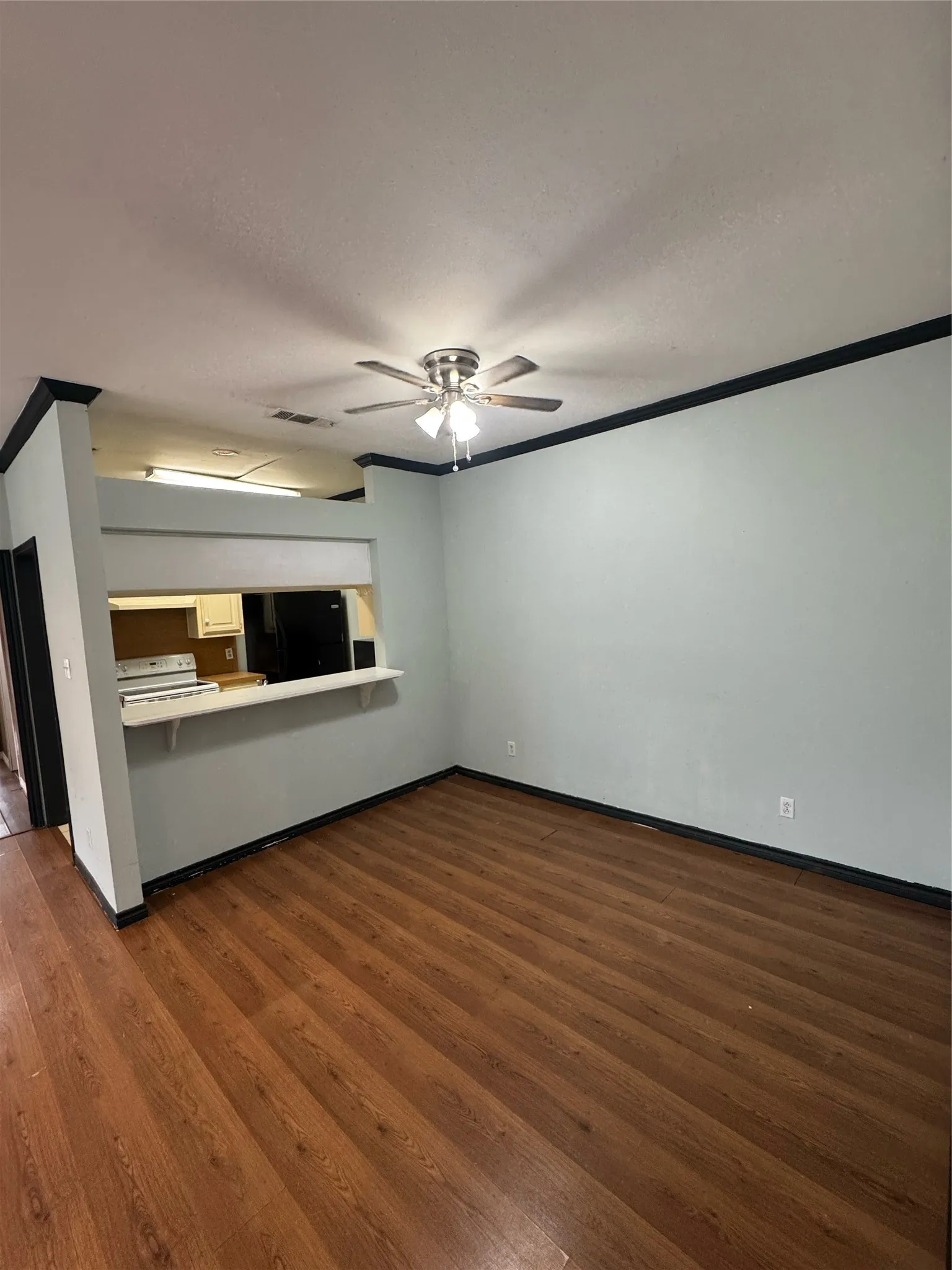 Expansive living area featuring rich wood-finish flooring, a ceiling fan with integrated lighting, and a pass-through opening to the kitchen