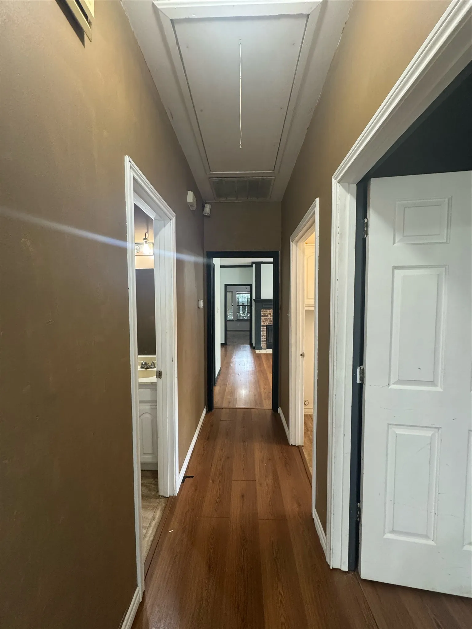 Hallway featuring wood-finish flooring, multiple doorways, and an overhead attic access panel