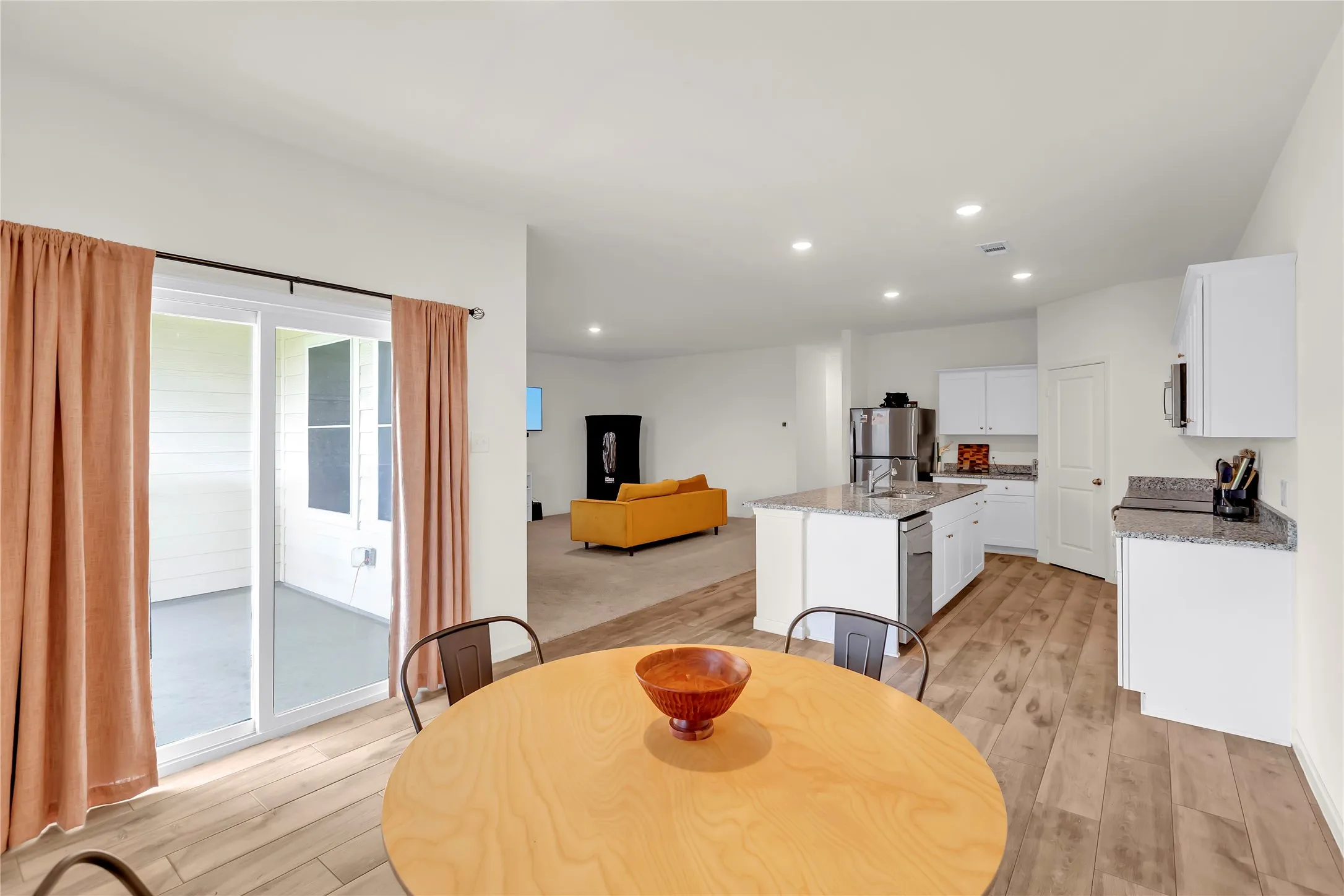 Open-concept kitchen and dining area featuring wood-finish flooring, white cabinetry, stainless steel appliances, recessed lighting, and granite countertops