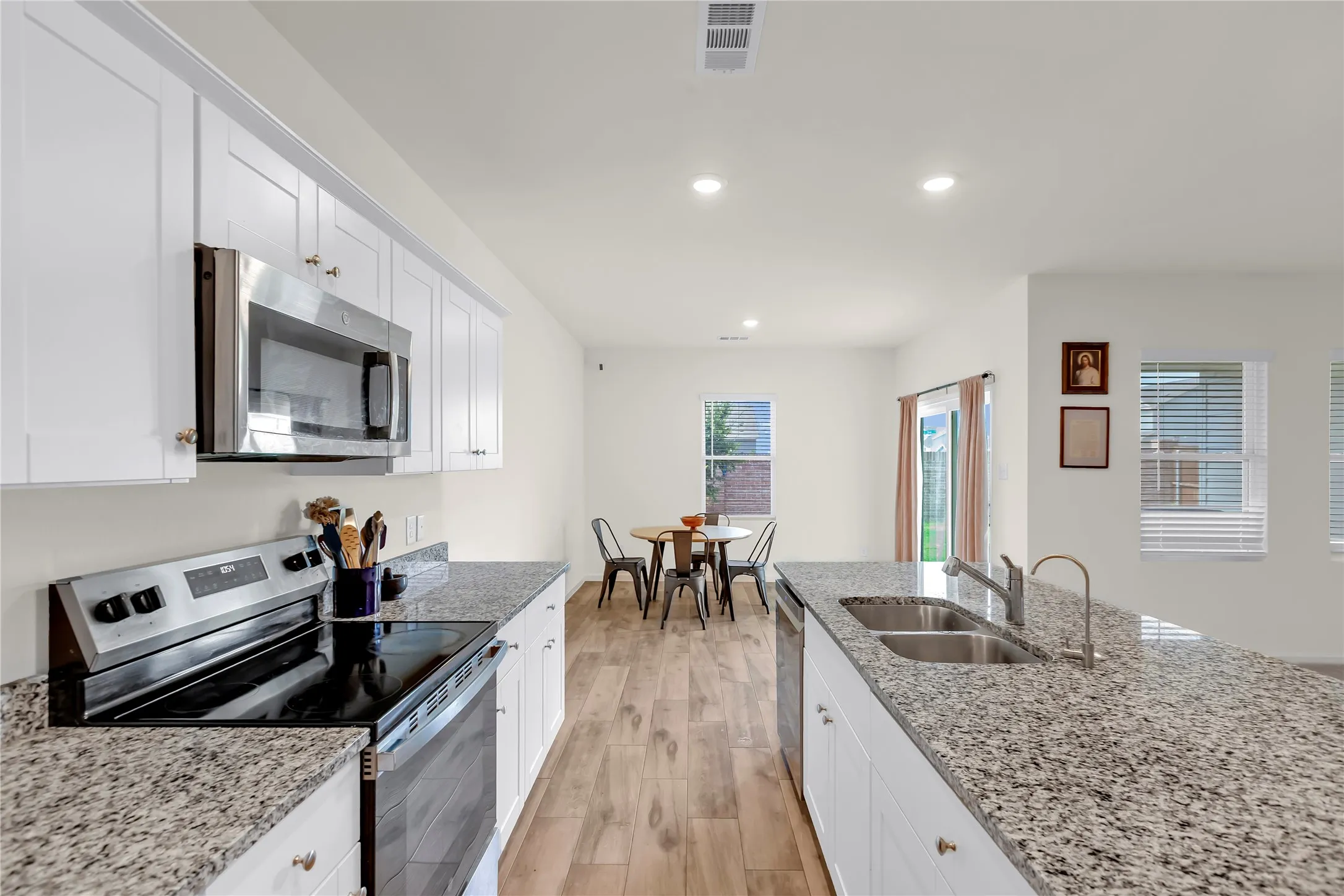 Kitchen featuring white cabinetry, stainless steel appliances, granite countertops, wood-finish flooring, and recessed lighting