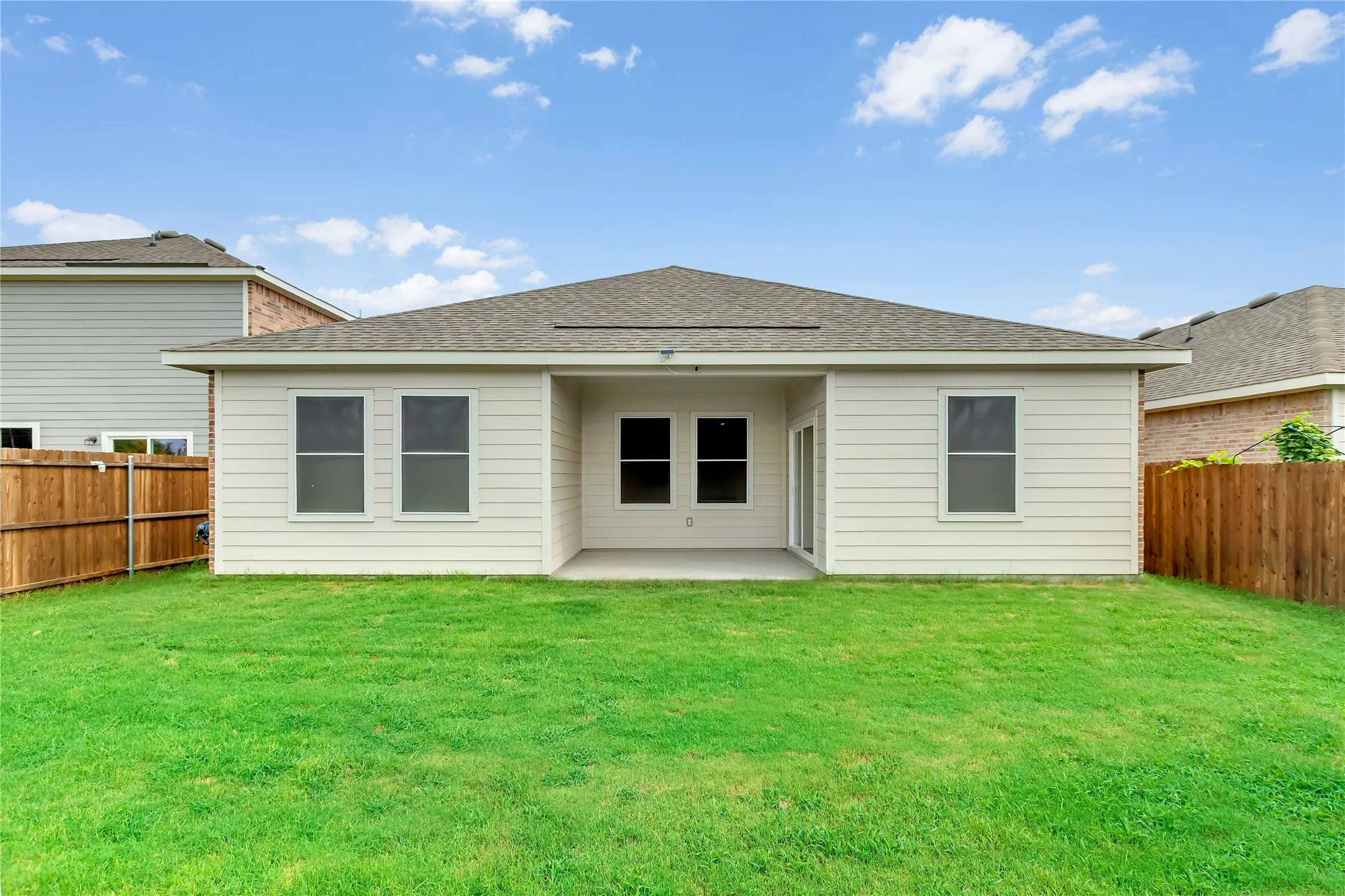 Expansive backyard featuring a lush lawn, privacy fencing, and a covered concrete patio