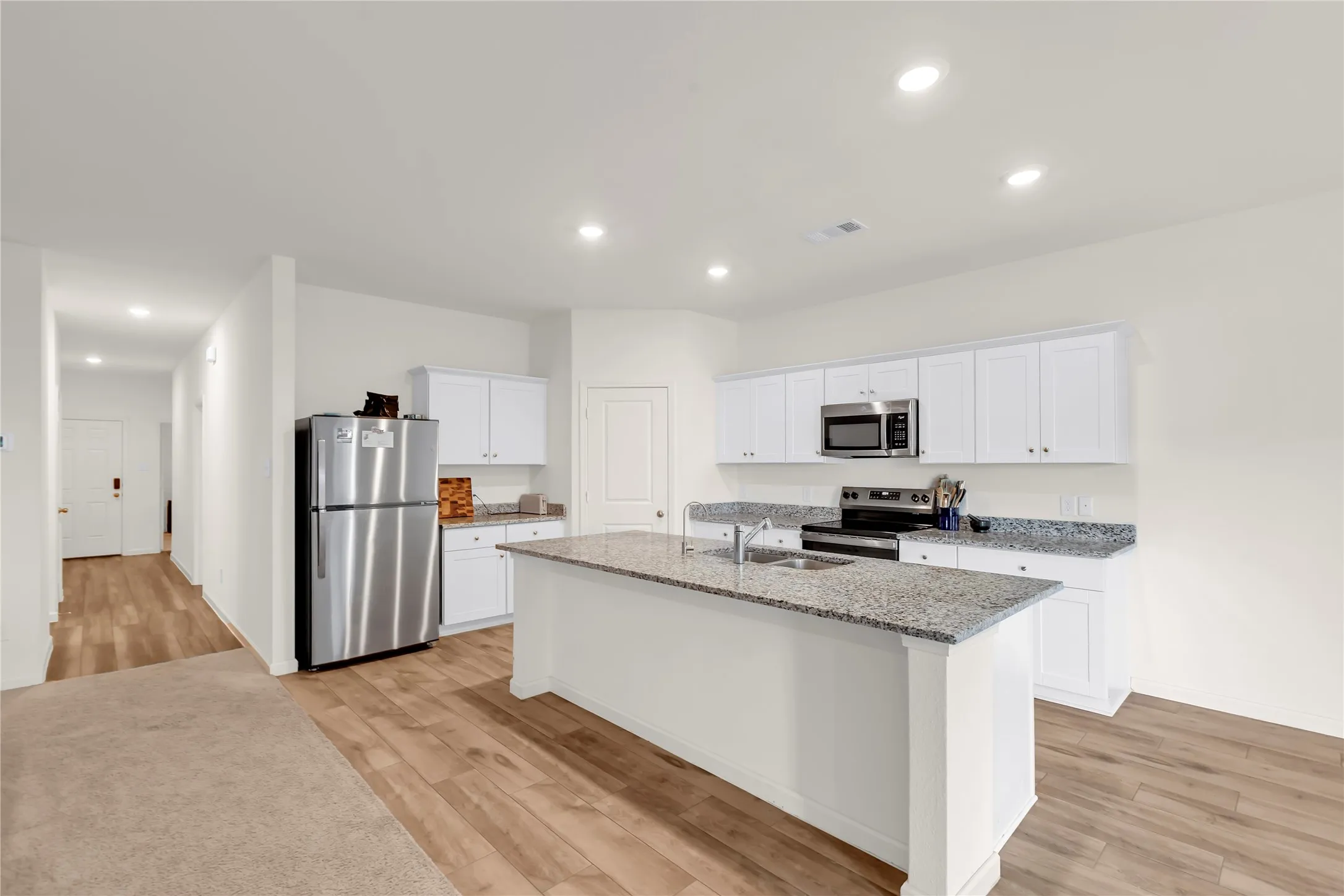 Modern kitchen featuring white cabinetry, granite countertops, stainless steel appliances, a center island with sink, and recessed lighting