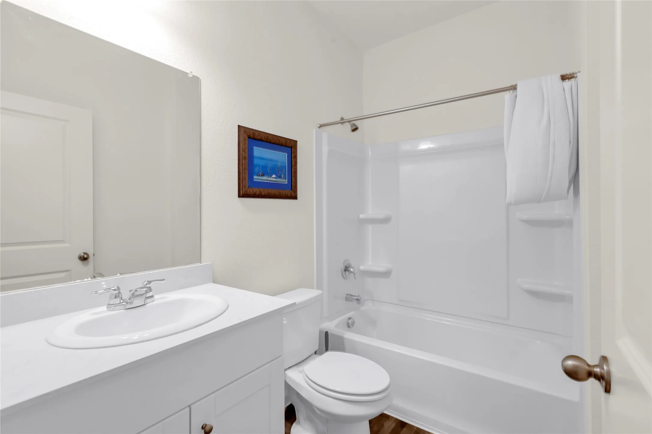 Bathroom featuring a white vanity with integrated sink, chrome faucet, wall-mounted mirror, and a white toilet