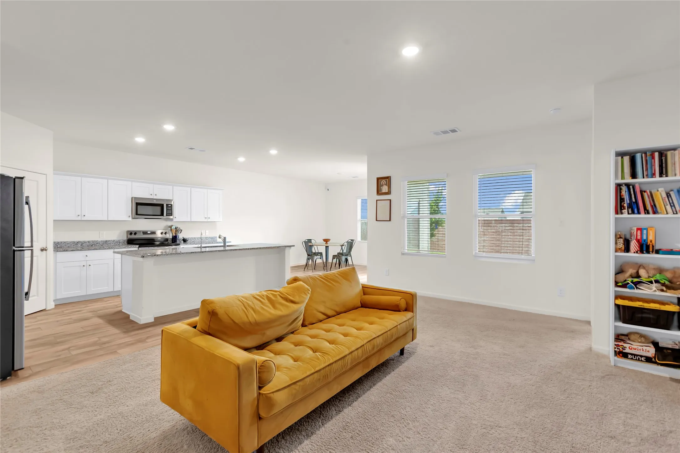 Open-concept living area featuring light-toned carpeting, recessed lighting, and multiple windows with blinds
