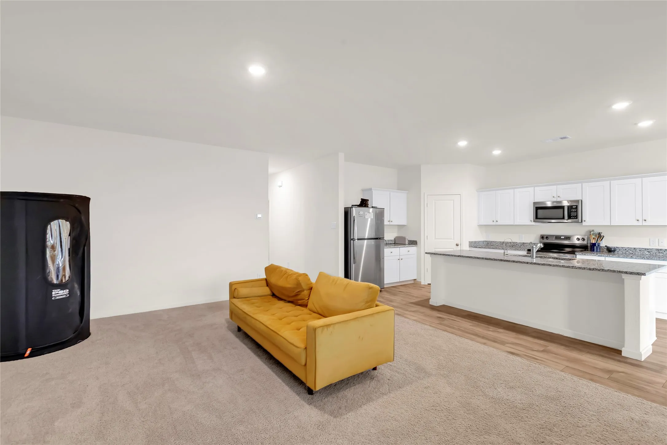 Open-concept living space featuring a modern kitchen with white cabinetry, stainless steel appliances, and granite countertops