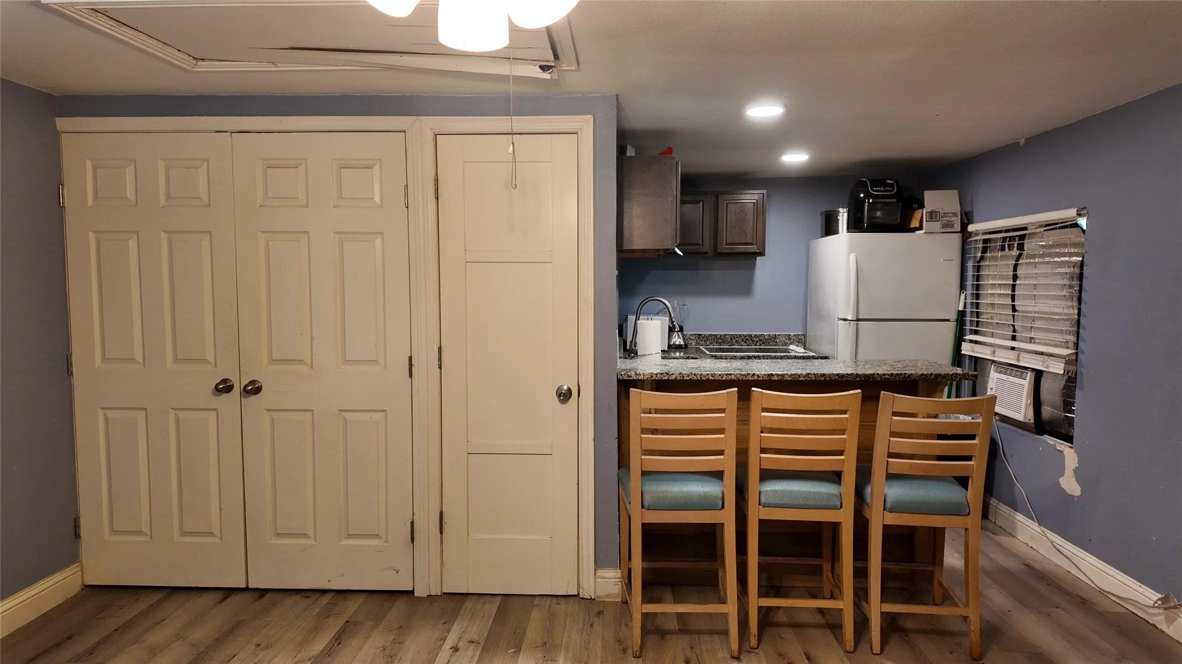 Compact kitchen area featuring wood-finish flooring, dark wood cabinetry, a built-in sink with a gooseneck faucet, a light-toned countertop, and recessed ceiling lighting