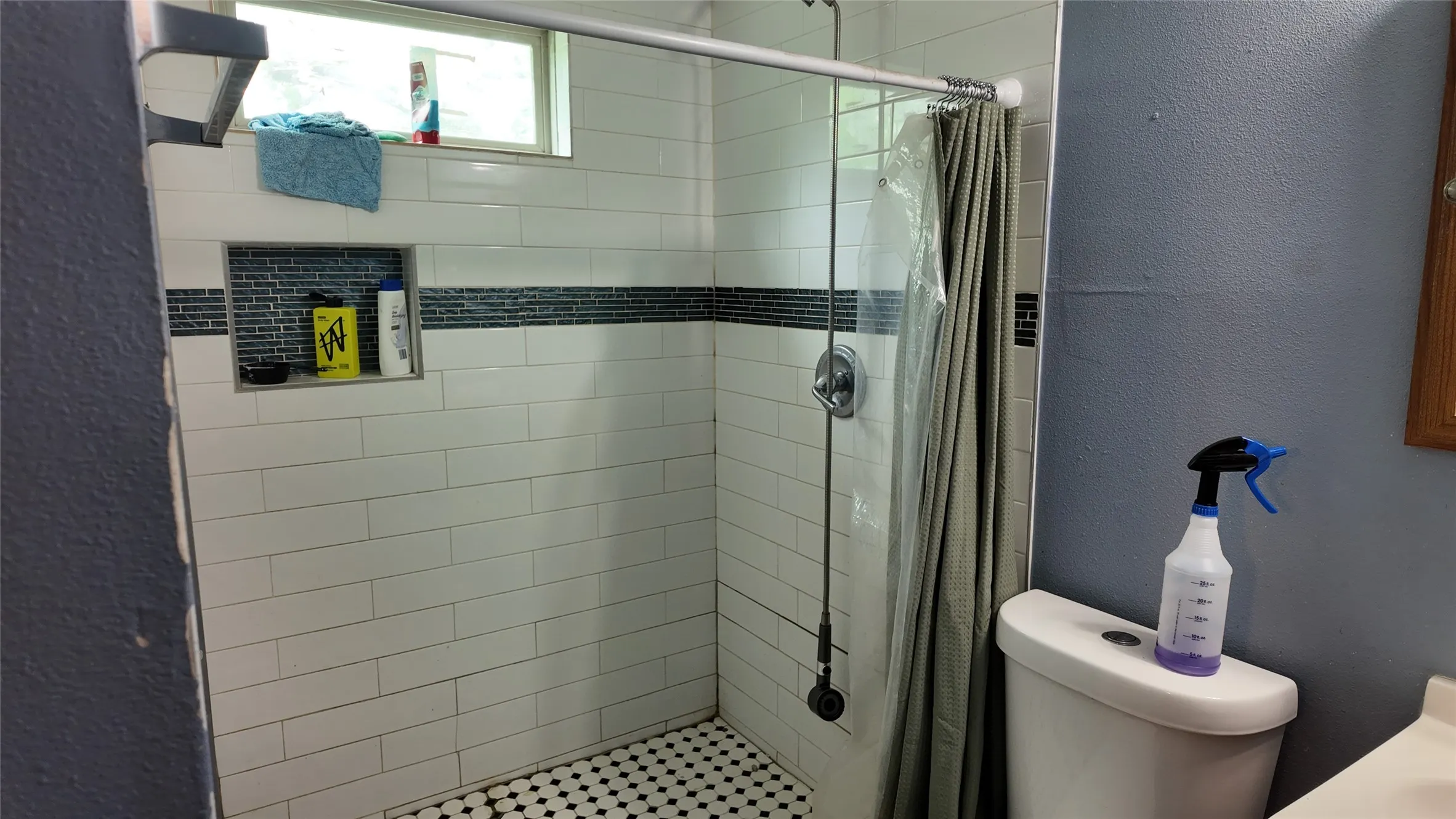 Shower enclosure featuring white subway tile, a dark accent tile band, and a hexagonal mosaic tile floor