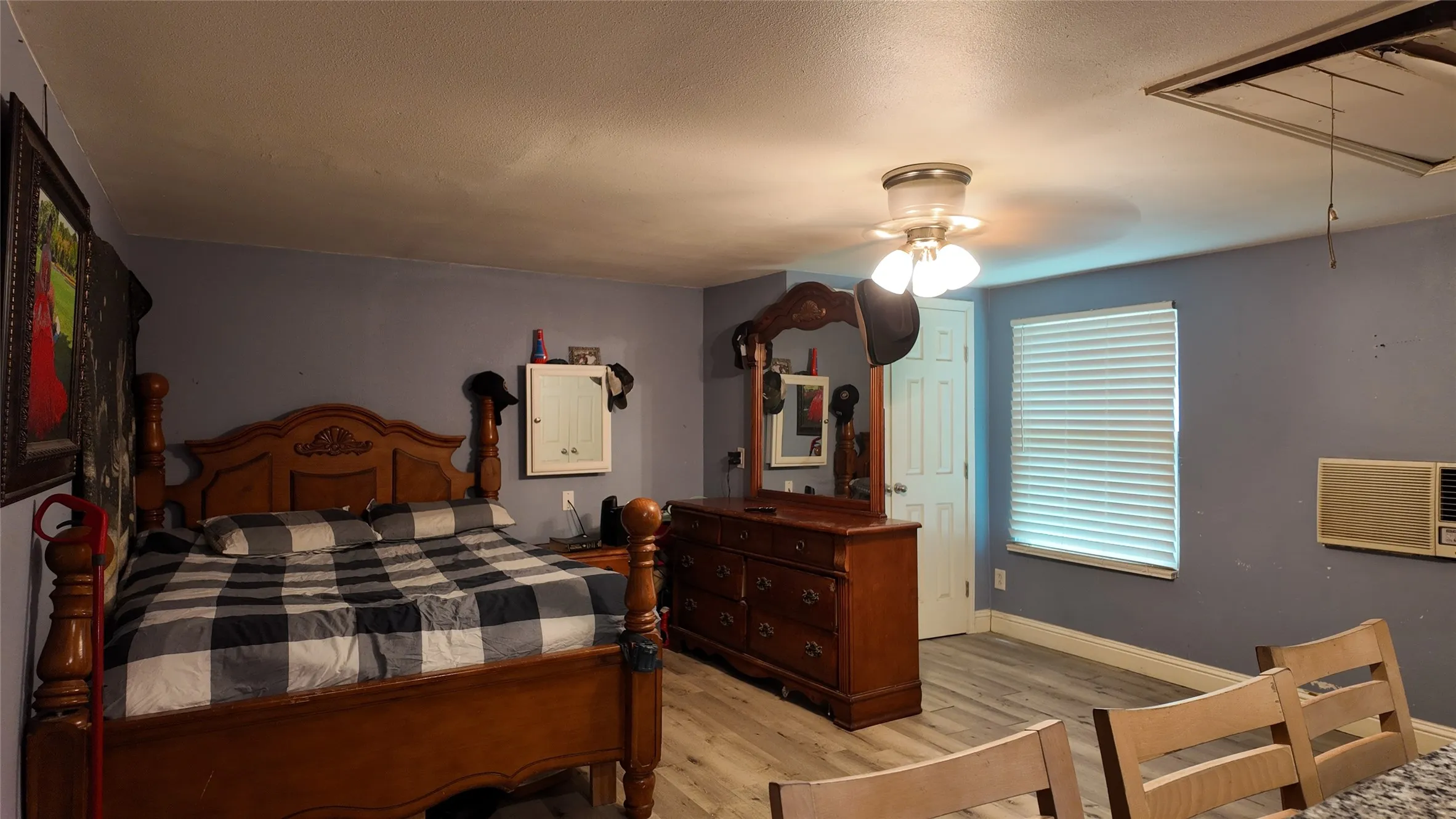 Spacious room featuring wood-finish flooring, a ceiling-mounted light fixture, and a window with horizontal blinds