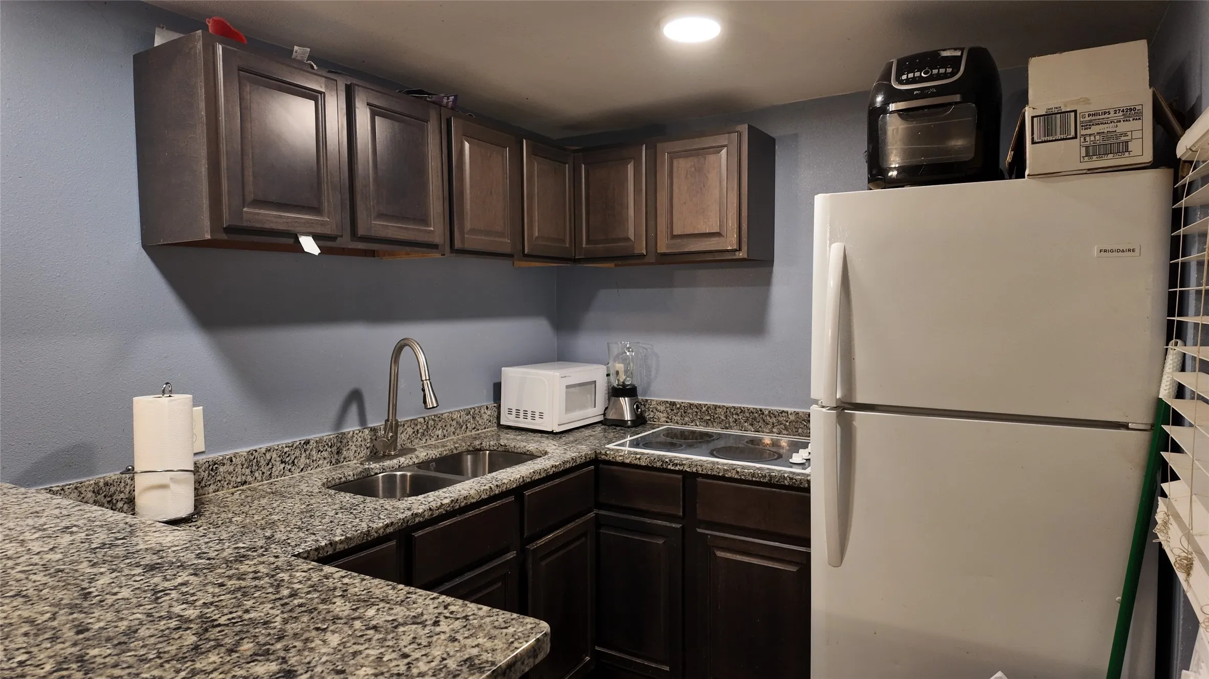 Kitchen featuring dark wood cabinetry, granite-style countertops, a double basin sink with a chrome faucet, and an electric cooktop