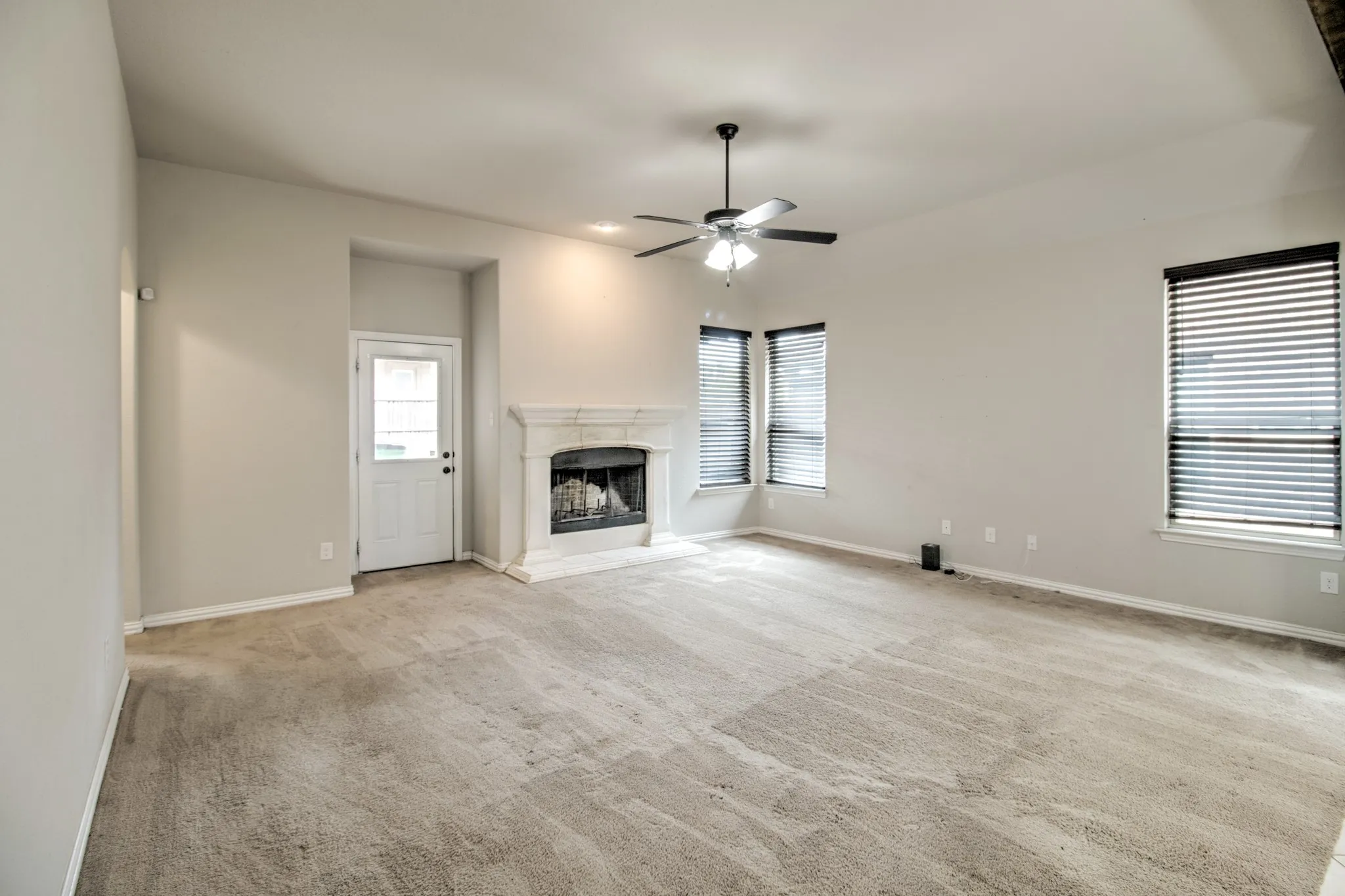 Spacious room featuring light-colored walls, patterned carpet, and a white paneled door