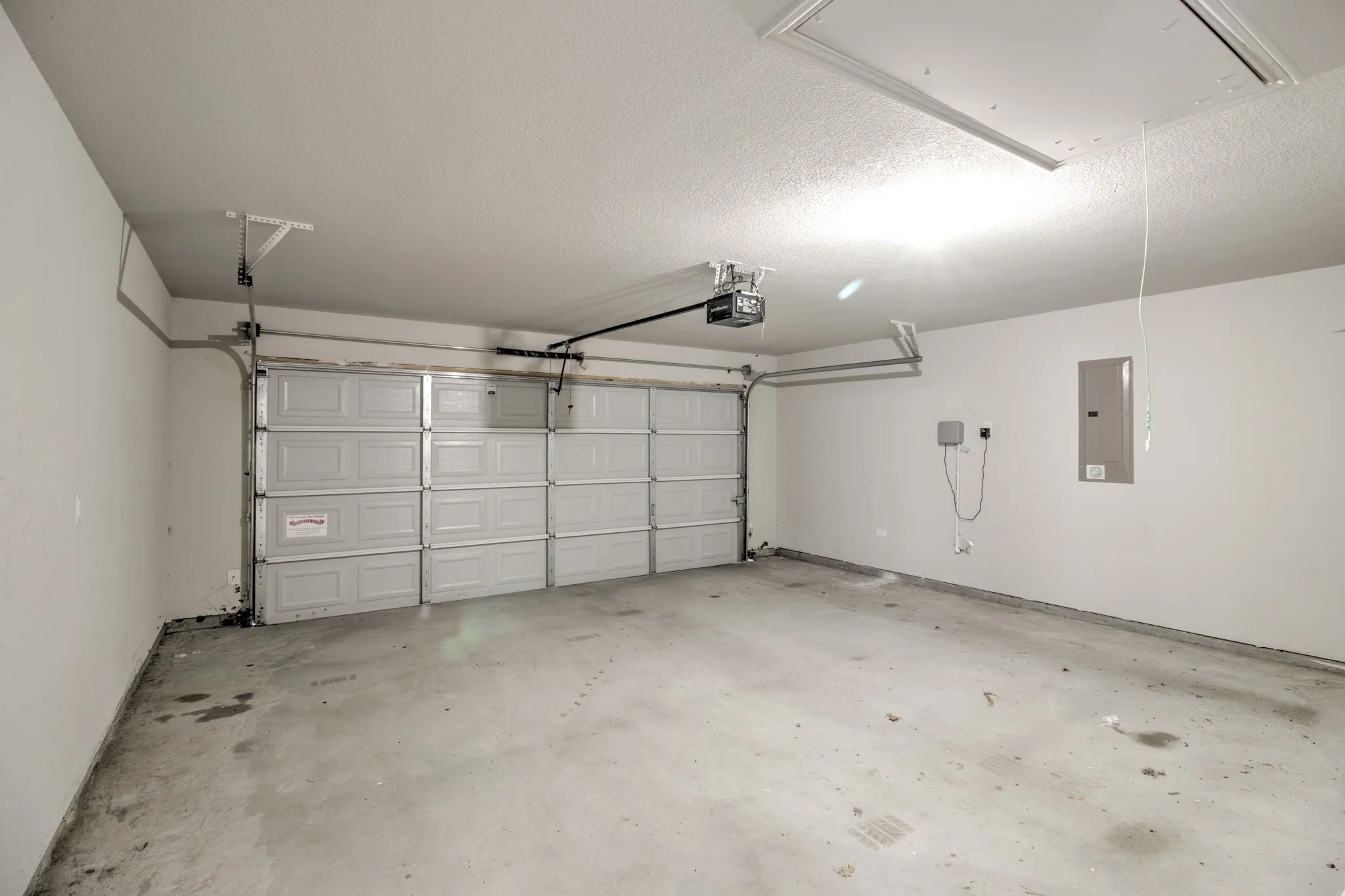 Two-car garage featuring a sectional garage door, concrete flooring, overhead lighting, and an access panel