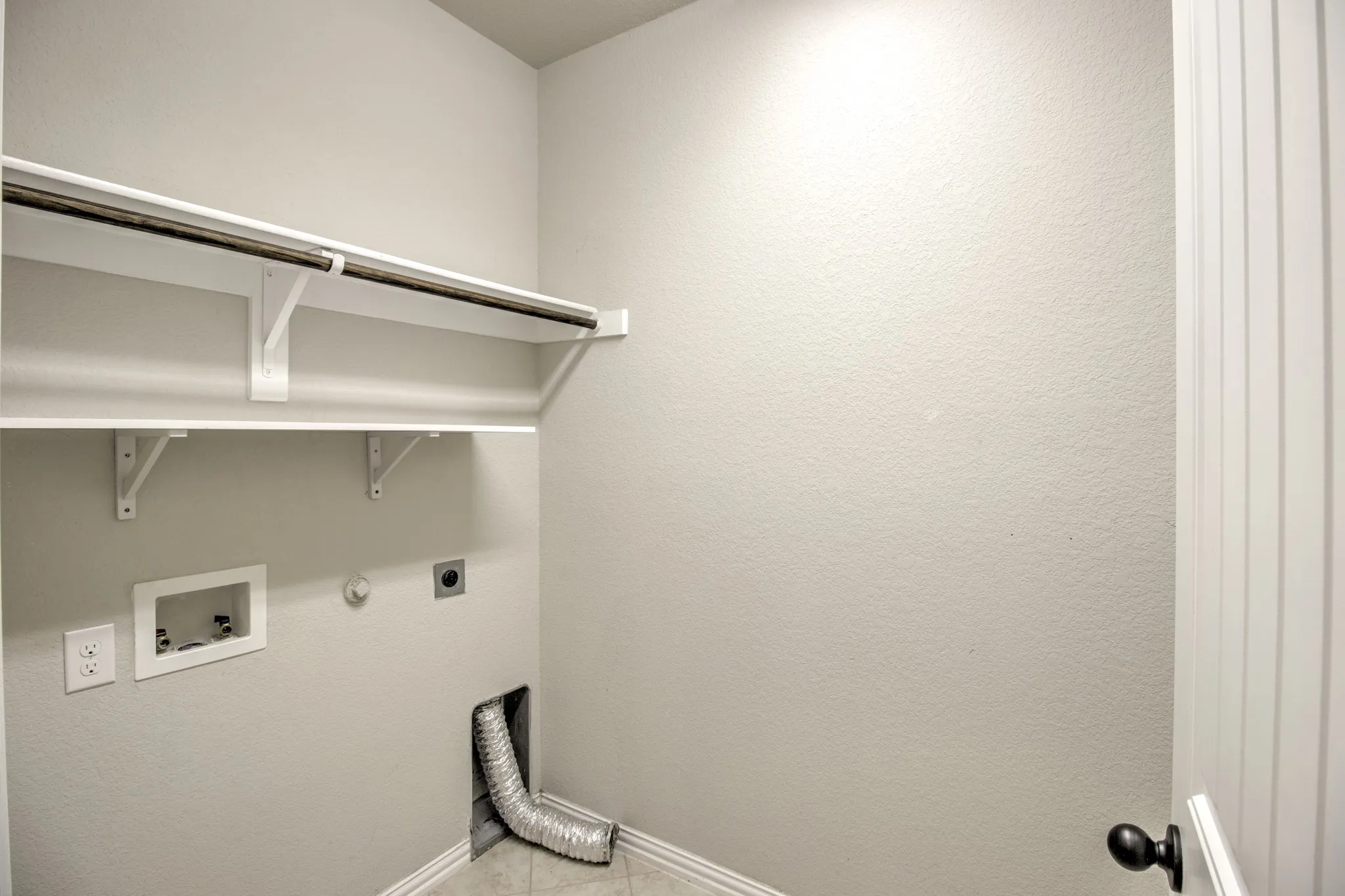 Dedicated laundry space featuring white shelving, a metal hanging rod, and textured walls