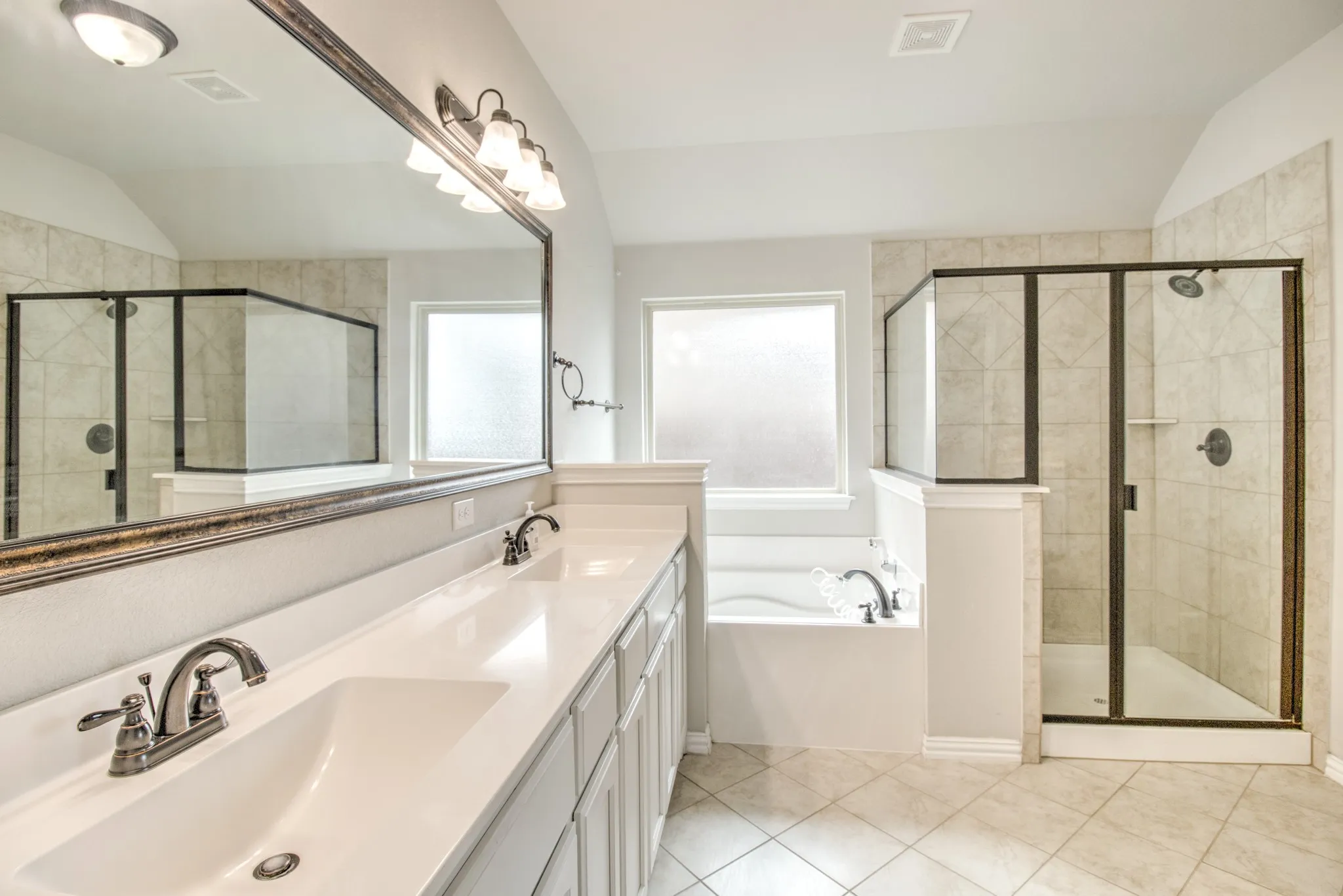 Spacious bathroom featuring a double vanity with white countertops, a large framed mirror, an enclosed glass shower, a separate bathtub, and tile flooring