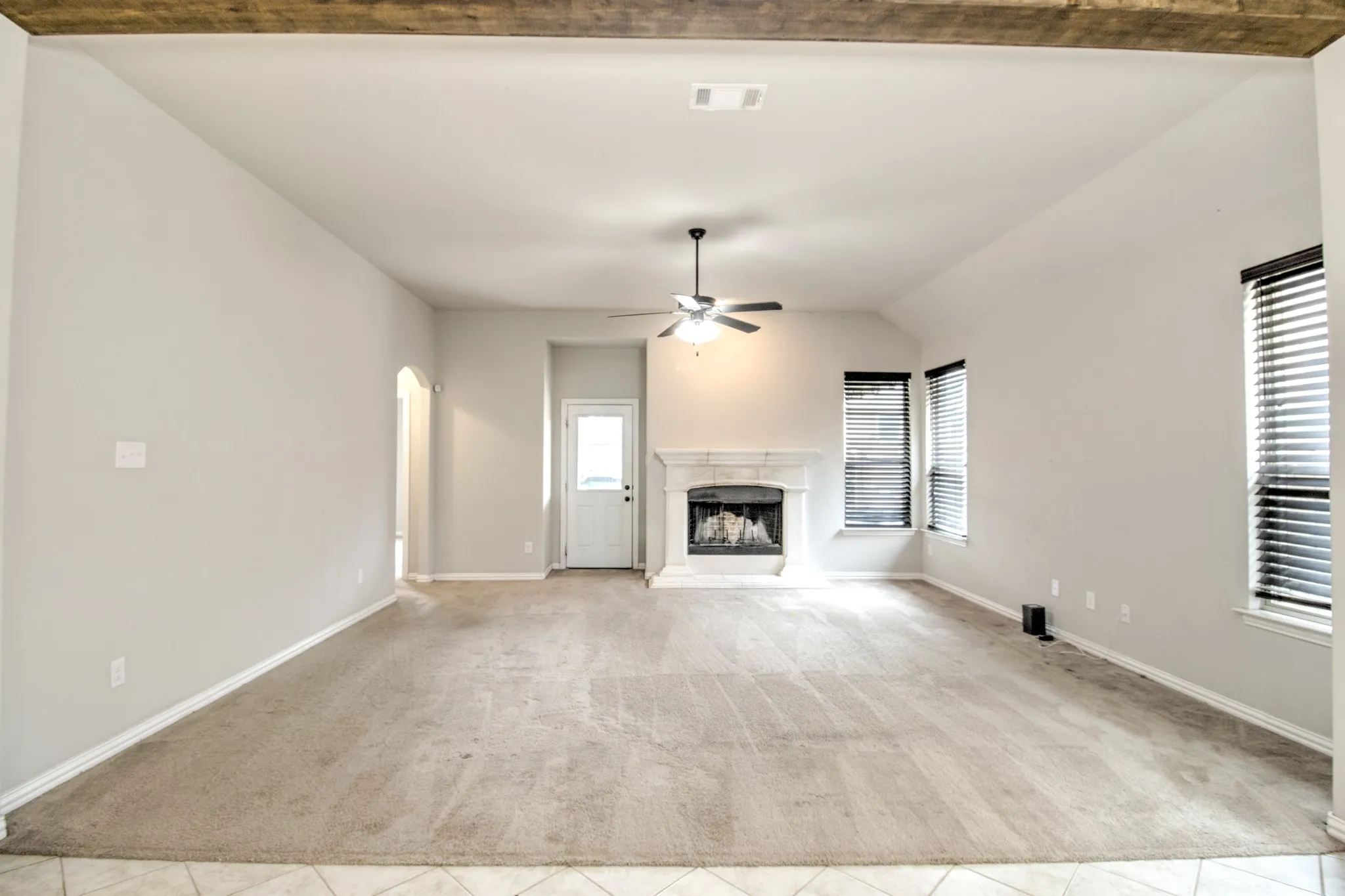 Spacious living area featuring a vaulted ceiling with a ceiling fan, a stone fireplace, and multiple windows with blinds