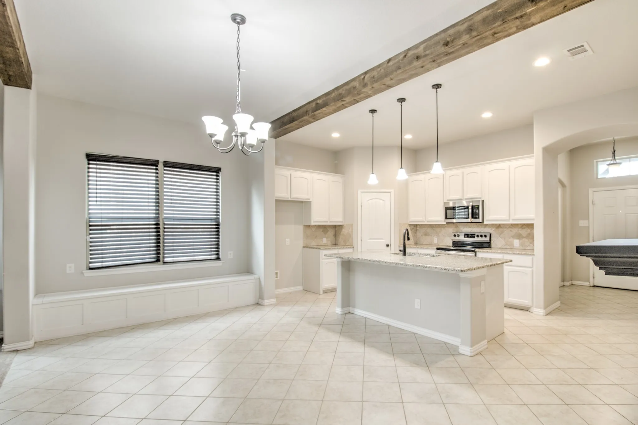 Open-concept living area featuring a kitchen island with pendant lighting, white cabinetry, stainless steel appliances, and tile flooring