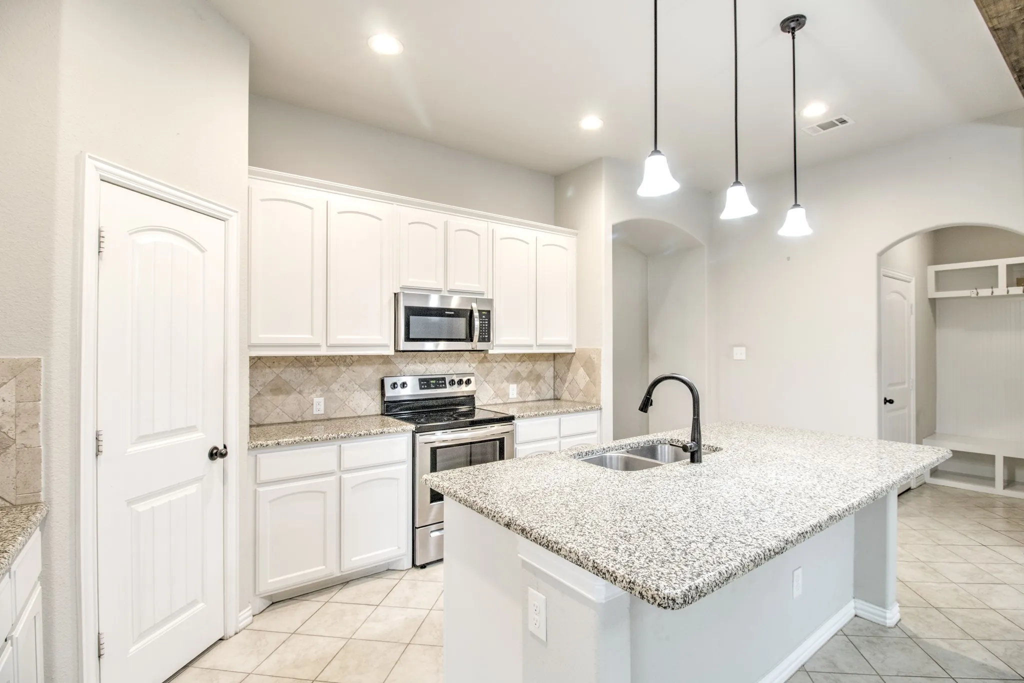 Gourmet kitchen featuring white cabinetry, stainless steel appliances, speckled countertops, a tile backsplash, and an island with a double basin sink and pendant lighting