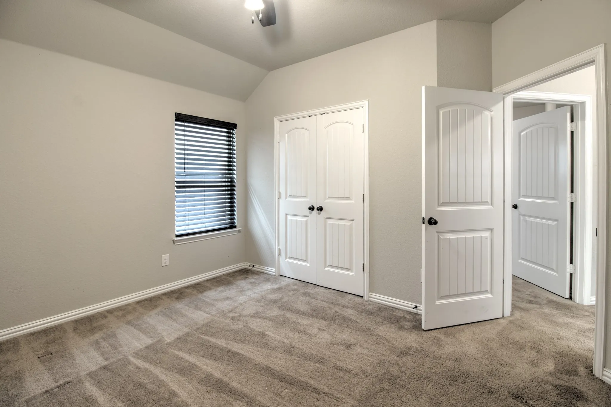 Carpeted interior room featuring light gray walls, white baseboards, and a window with black blinds