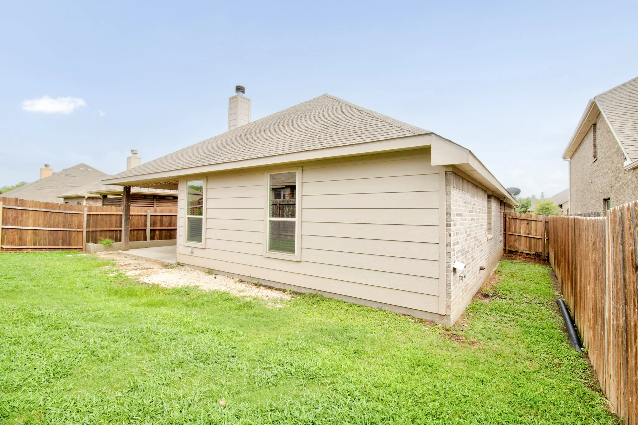 Rear exterior featuring a covered patio, wood privacy fencing, and a combination of brick and siding finishes
