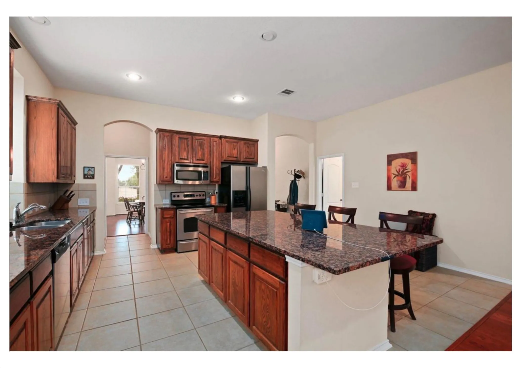 Kitchen featuring a large island with a stone countertop, rich wood cabinetry, stainless steel appliances, recessed lighting, and tile flooring