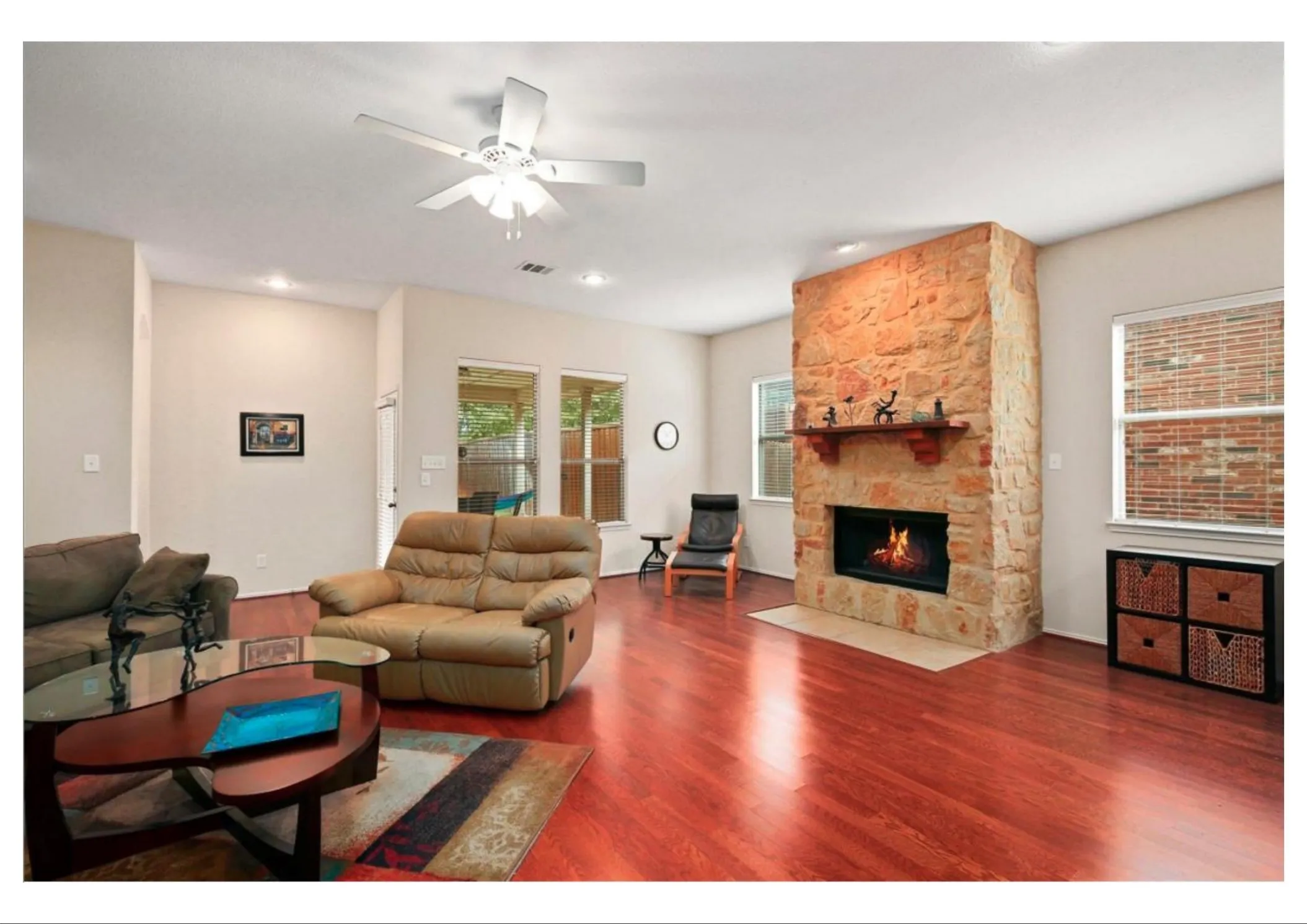 Living area featuring a stone-clad fireplace with mantel, two large windows, wood-finish flooring, and recessed lighting