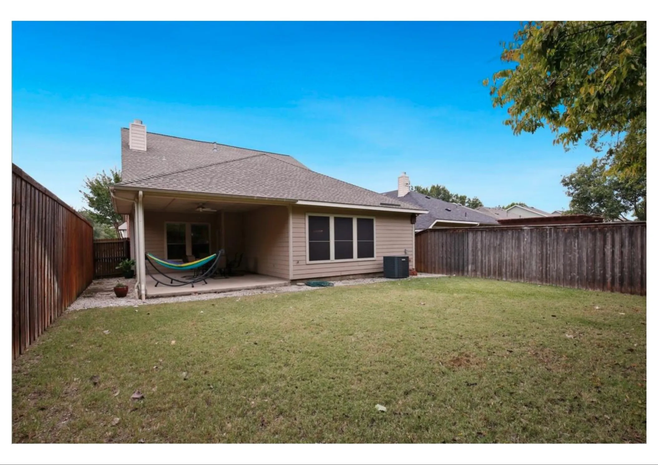 Expansive backyard featuring a covered patio, manicured lawn, and privacy fencing