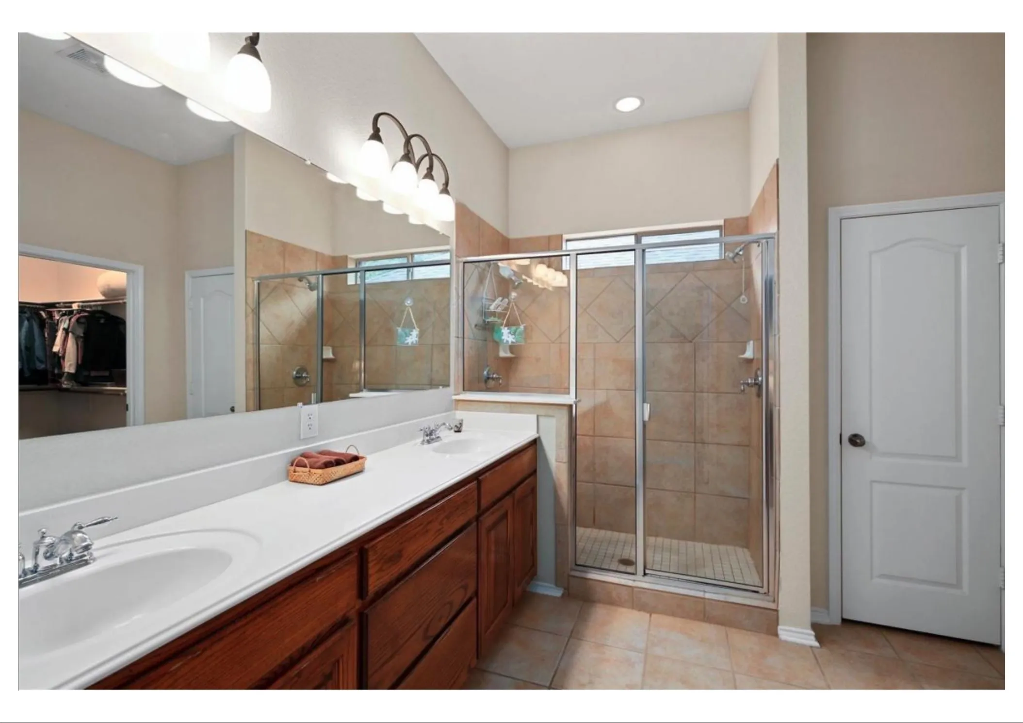 Bathroom featuring a dual vanity with white countertop, wood-finish cabinetry, and a full-width mirror