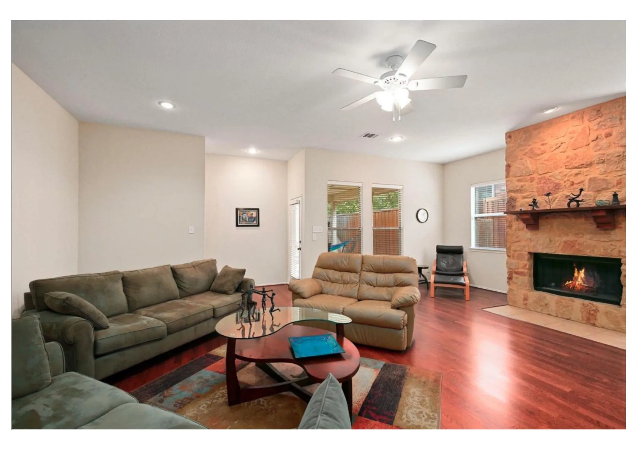 Living area featuring rich wood-finish flooring, a stone-clad fireplace with a hearth, recessed lighting, and a ceiling fan