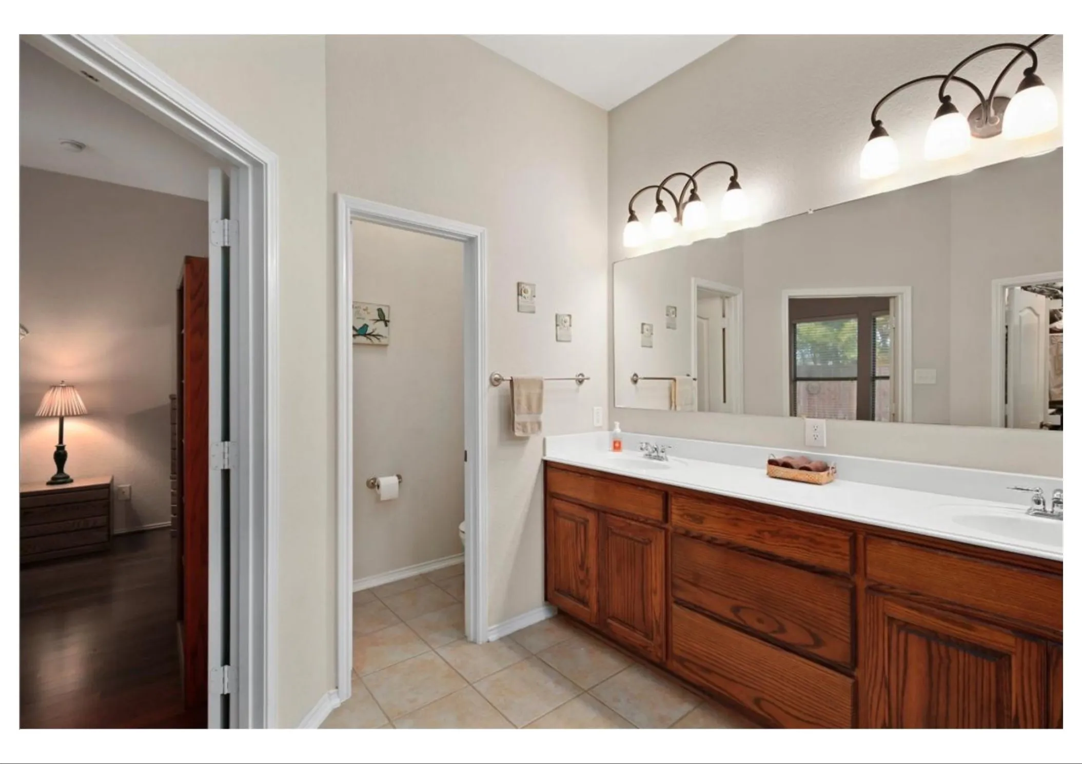 Dual sink vanity with wood-finish cabinetry, a white countertop, and extensive wall-mounted mirror