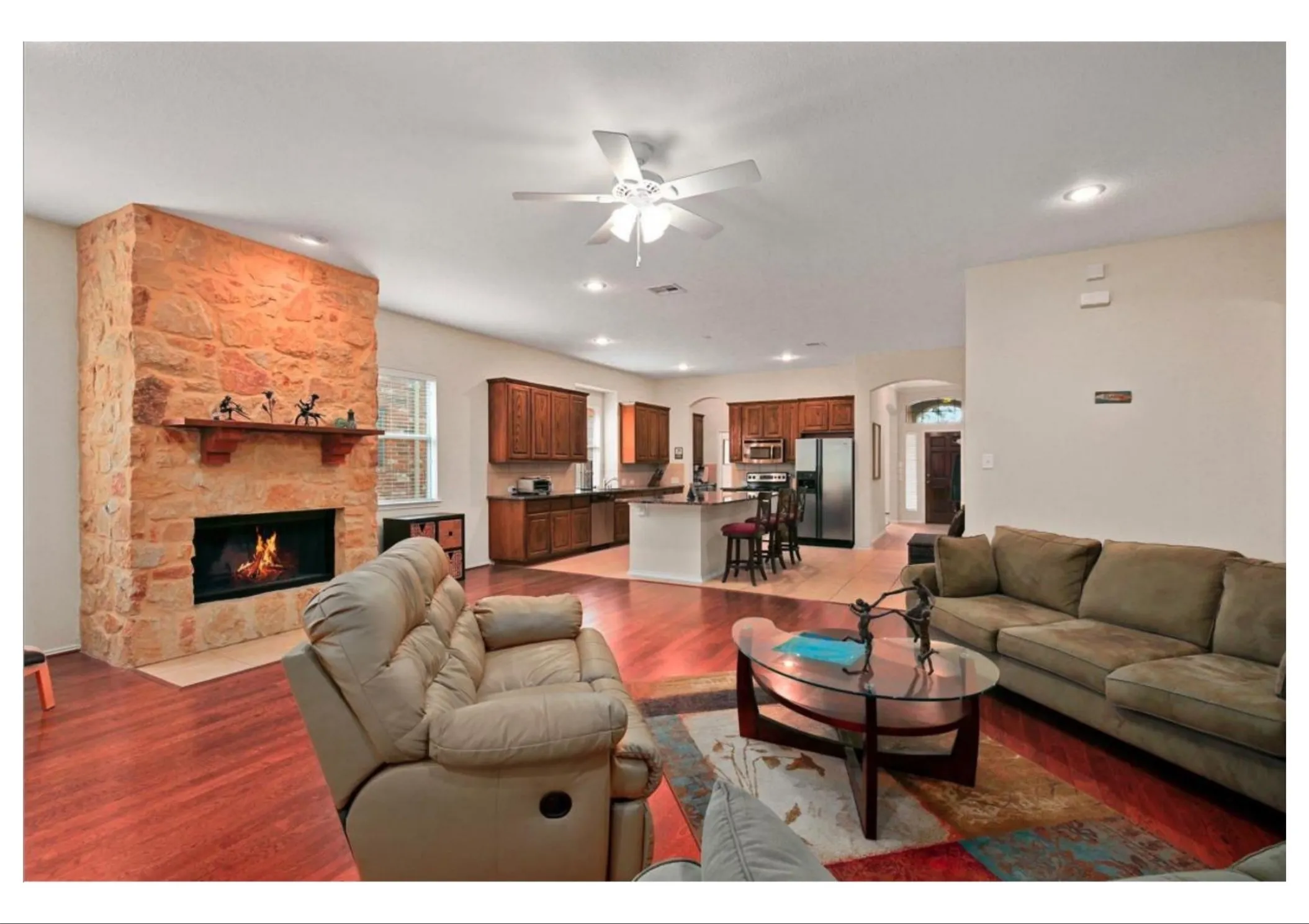 Open-concept living area featuring wood-finish flooring and a stone-clad fireplace with a wood mantle