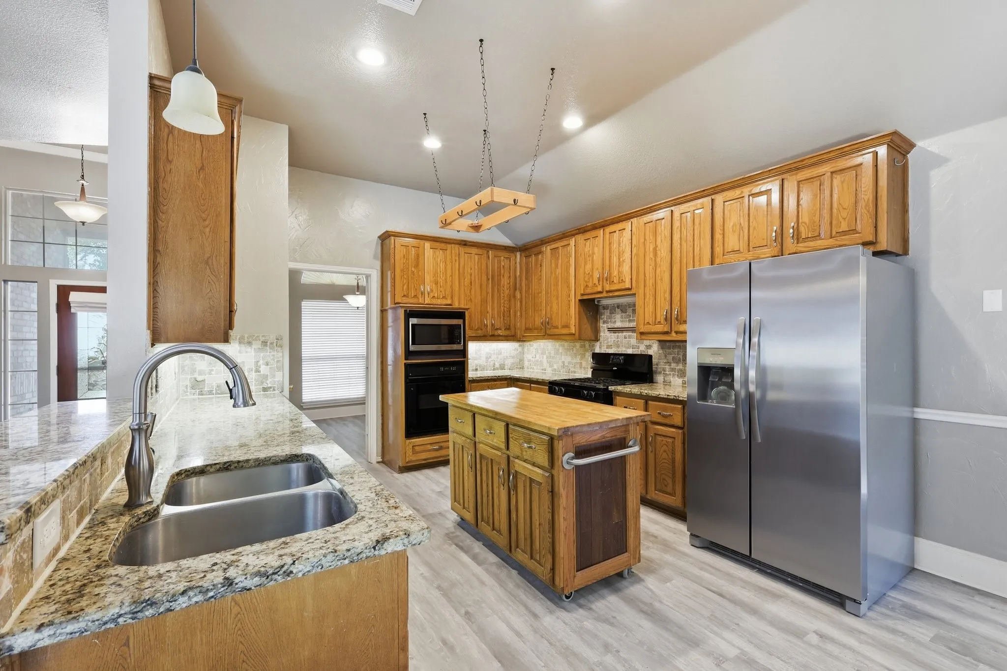 Kitchen featuring wood-finish cabinetry, granite countertops, a stainless steel double sink, and a central island with wood-finish top