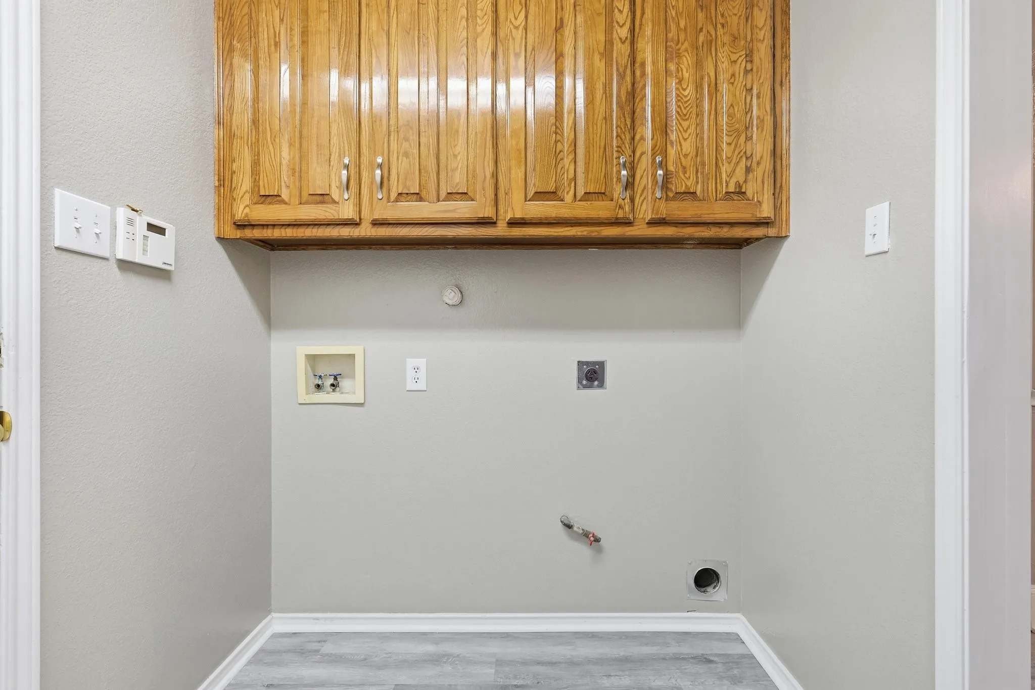 Dedicated laundry area featuring overhead wood cabinetry with silver hardware, light gray walls, and wood-finish flooring