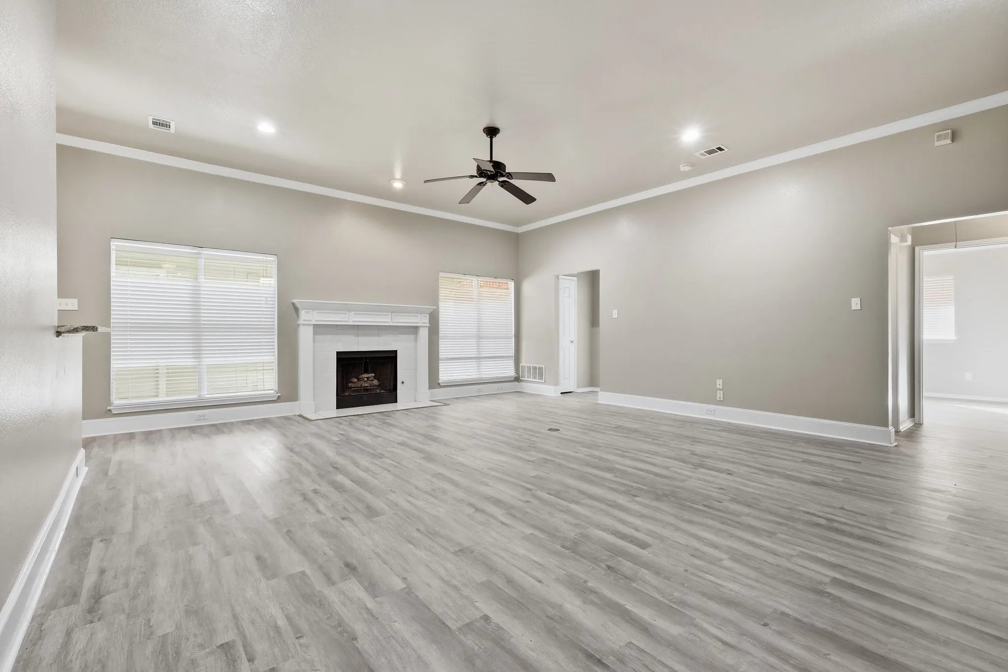 Spacious living area featuring light gray wood-finish flooring, a white mantel fireplace, and a ceiling fan