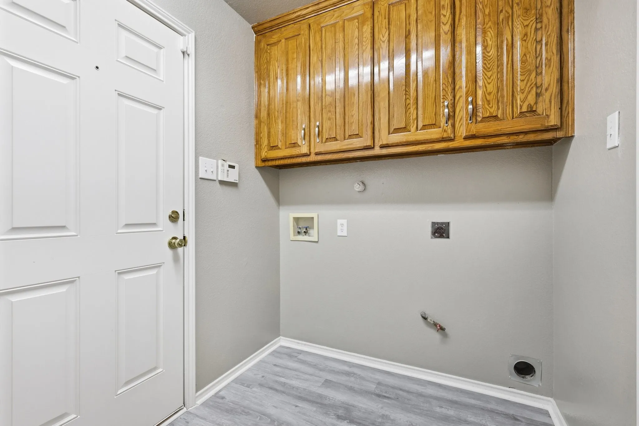 Utility area featuring overhead wood cabinetry and wood-finish flooring