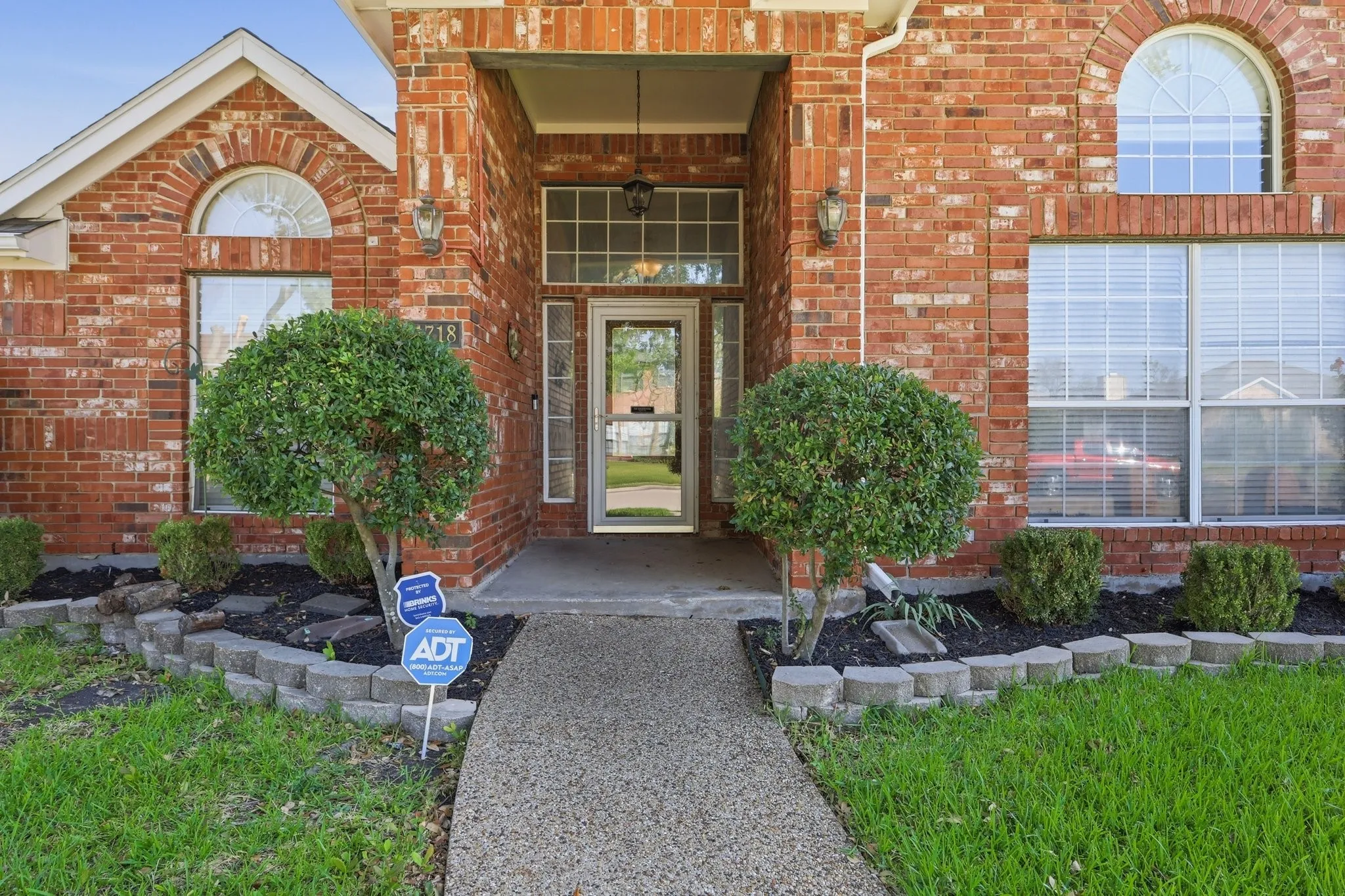 Brick facade exterior featuring a covered entry, arched window accents, and an aggregate concrete walkway
