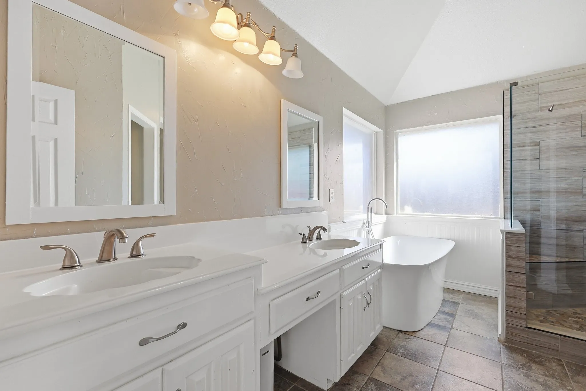 Bathroom featuring a freestanding soaking tub, enclosed glass shower, double vanity, vaulted ceiling, and rectangular floor tiles