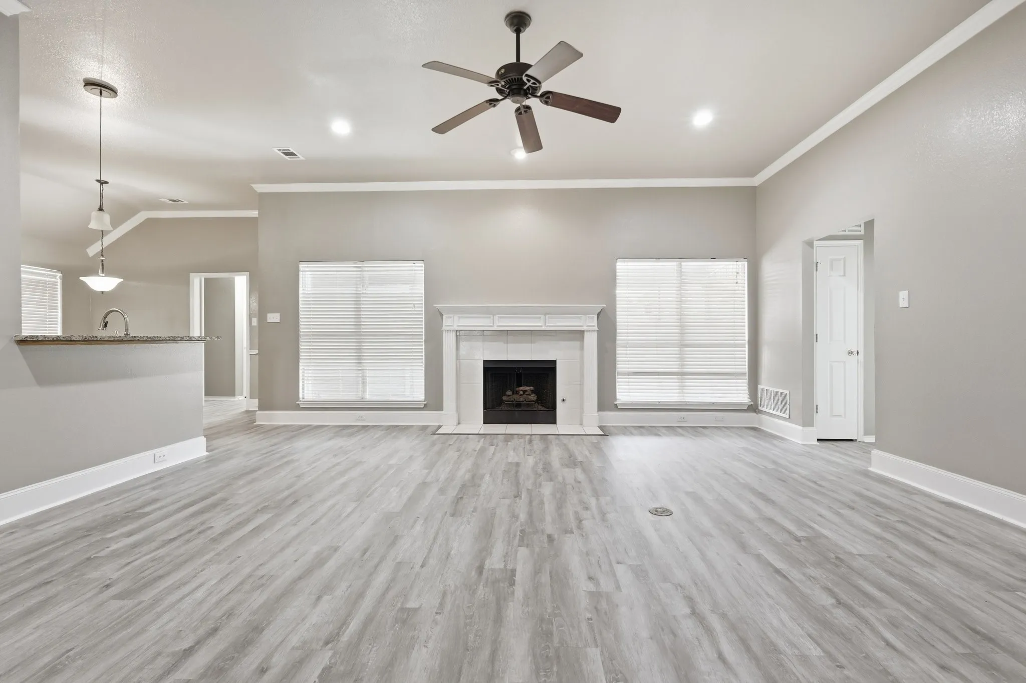 Spacious living area featuring wood-finish flooring, a decorative fireplace with a mantel, and crown molding