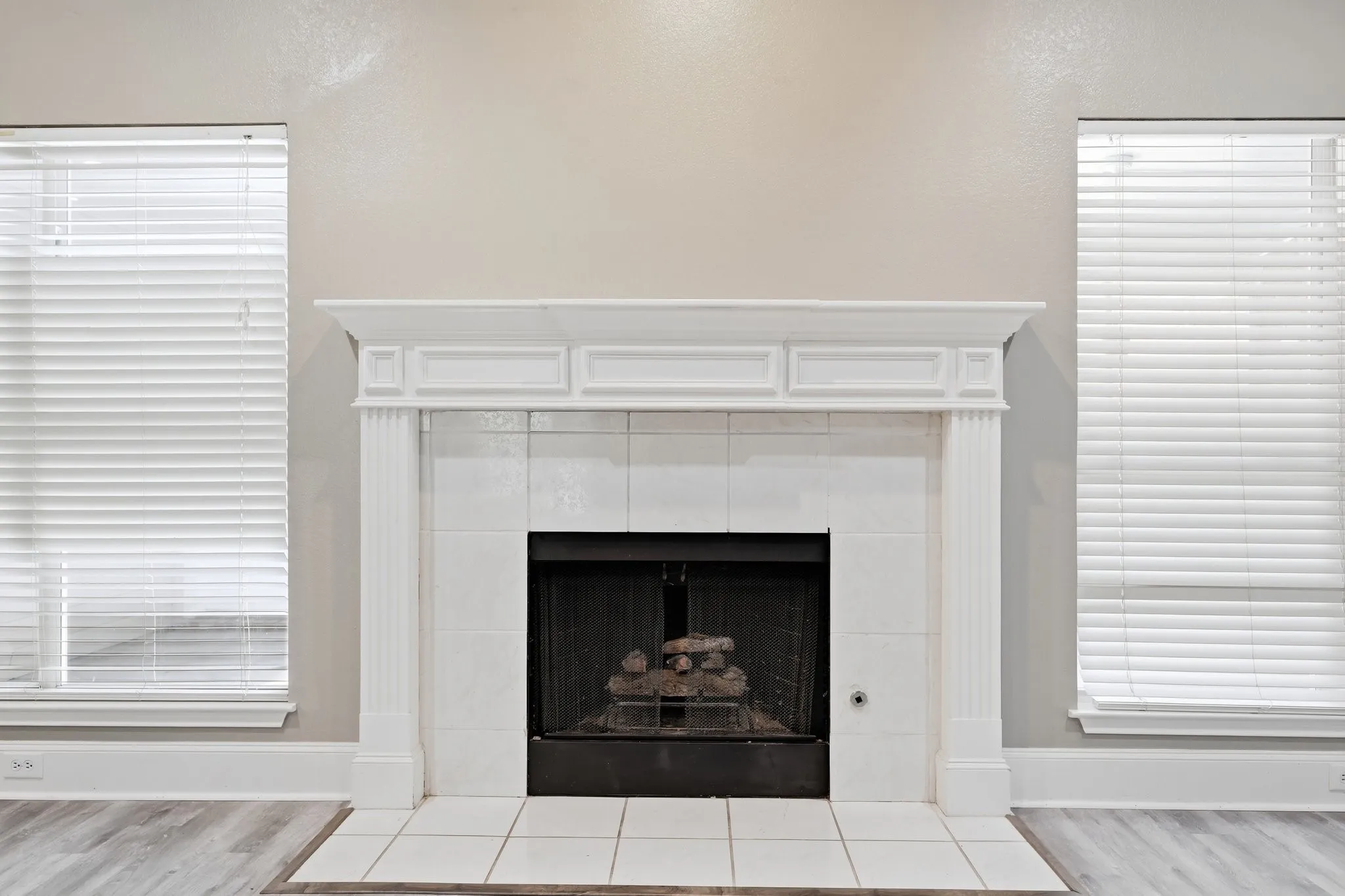 Fireplace with a white mantel and hearth, flanked by two windows with white blinds