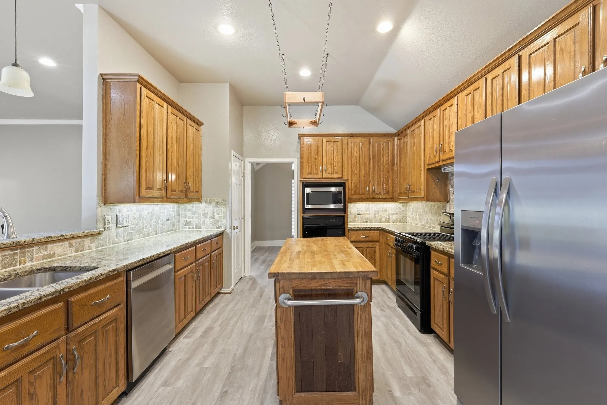 Kitchen featuring wood cabinetry, stainless steel appliances, granite countertops, a tile backsplash, and light wood-finish flooring