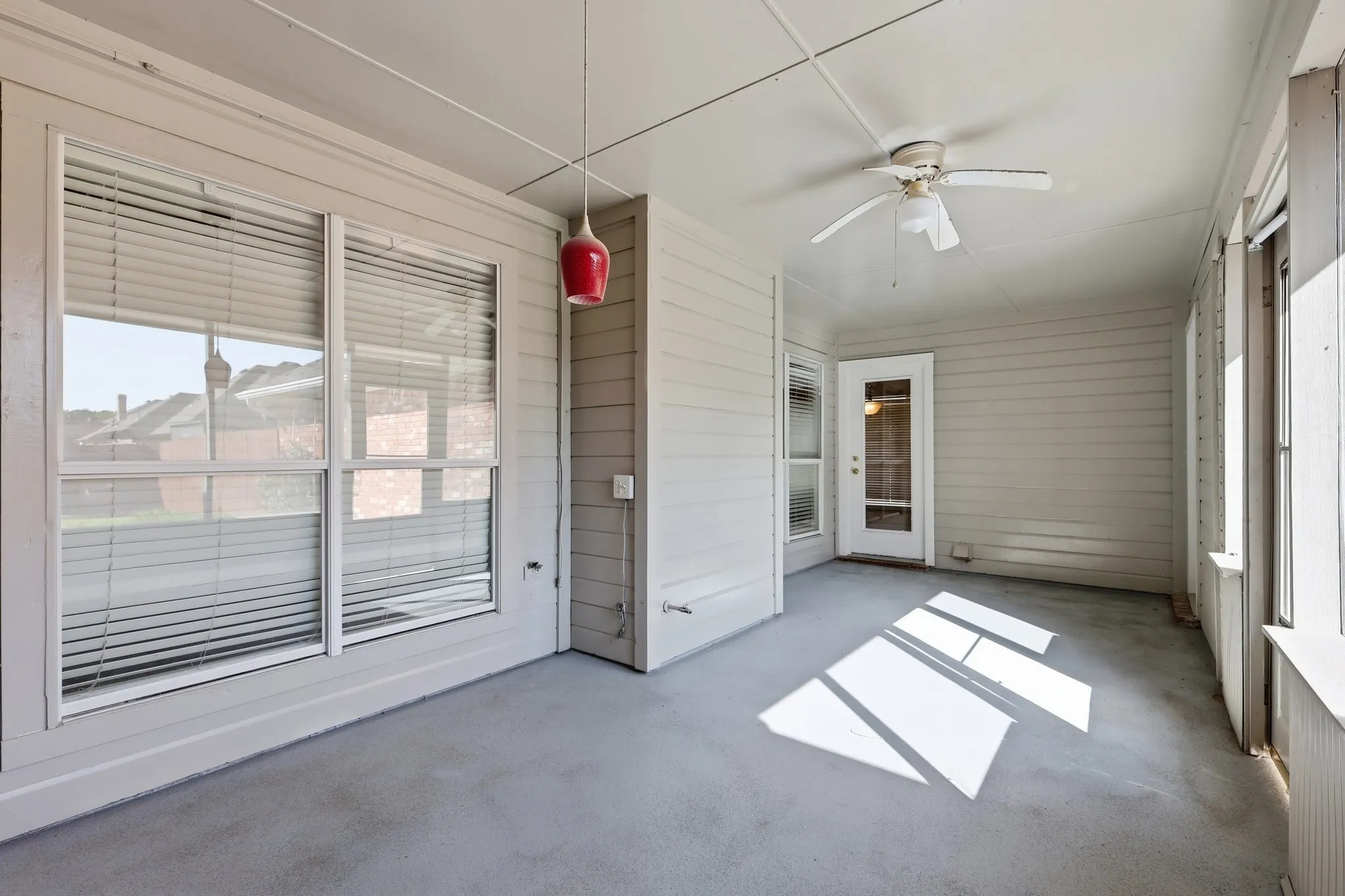 Enclosed sunroom featuring a ceiling fan, a white exterior door, multiple windows with blinds, and a smooth concrete floor