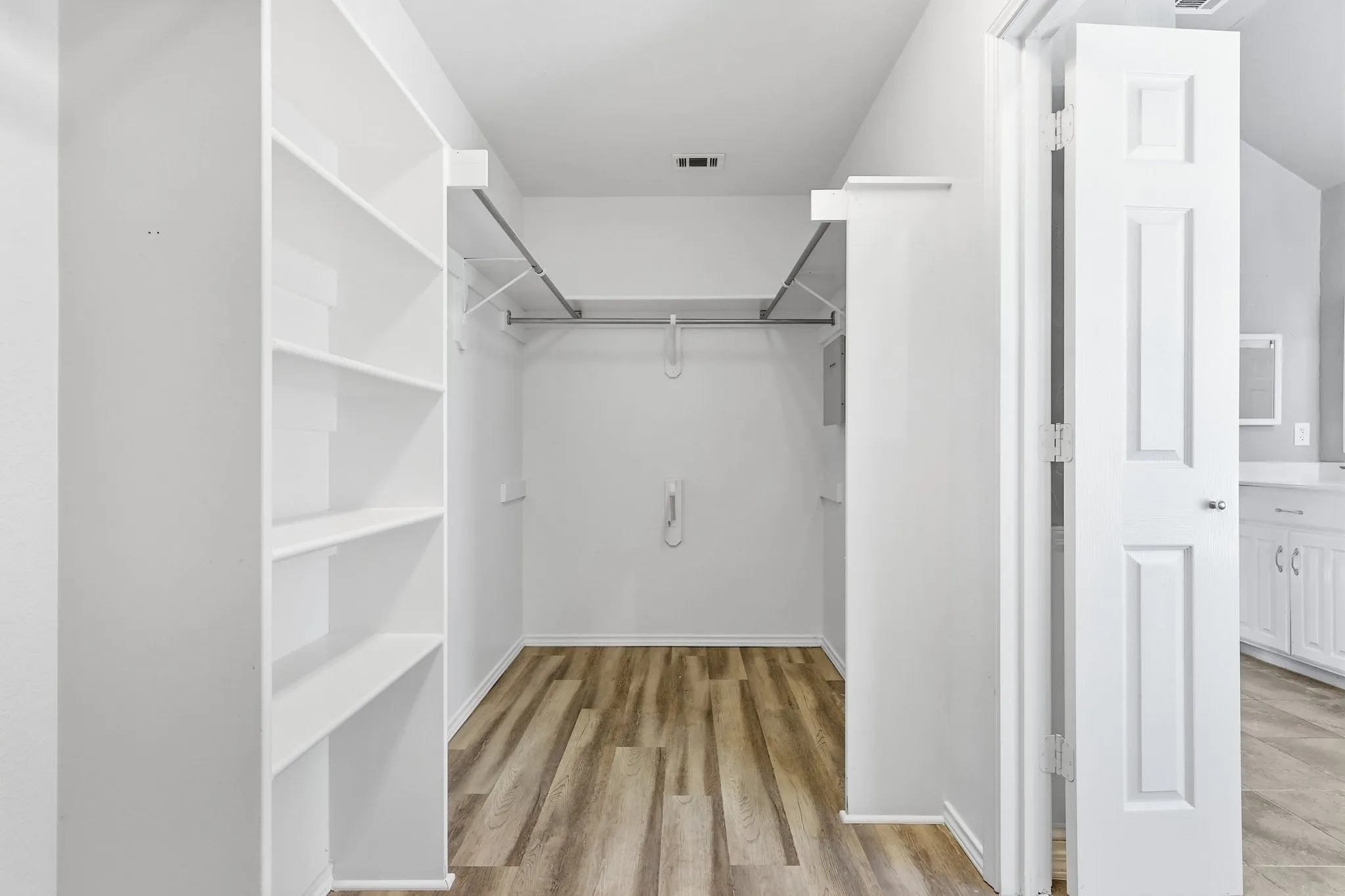 Walk-in closet featuring built-in shelving, hanging rods, wood-finish flooring, and a paneled door