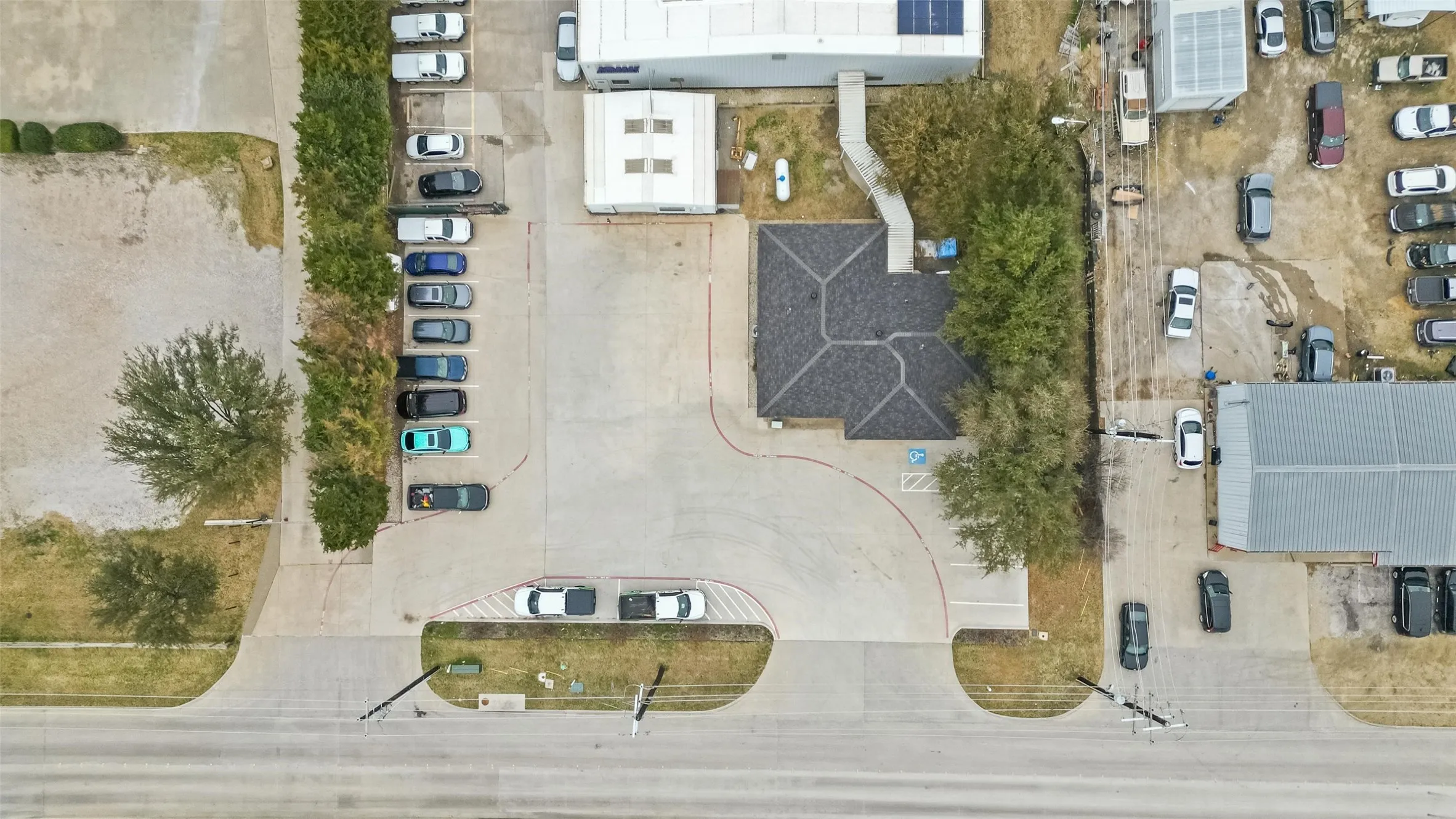 Aerial perspective showcasing a commercial property with a paved parking area and a main building featuring a dark shingle roof