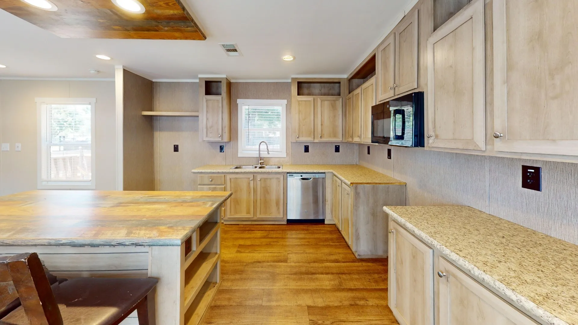 Kitchen featuring wood-finish flooring, light wood-tone cabinetry, a peninsula with a patterned countertop, a built-in microwave, and a stainless steel dishwasher