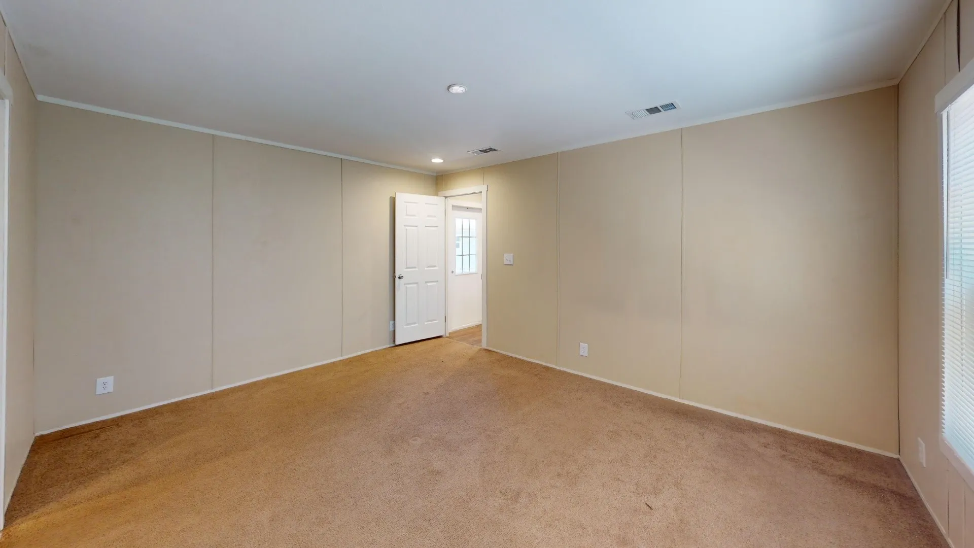 Spacious room featuring neutral carpeting and light-toned wall paneling