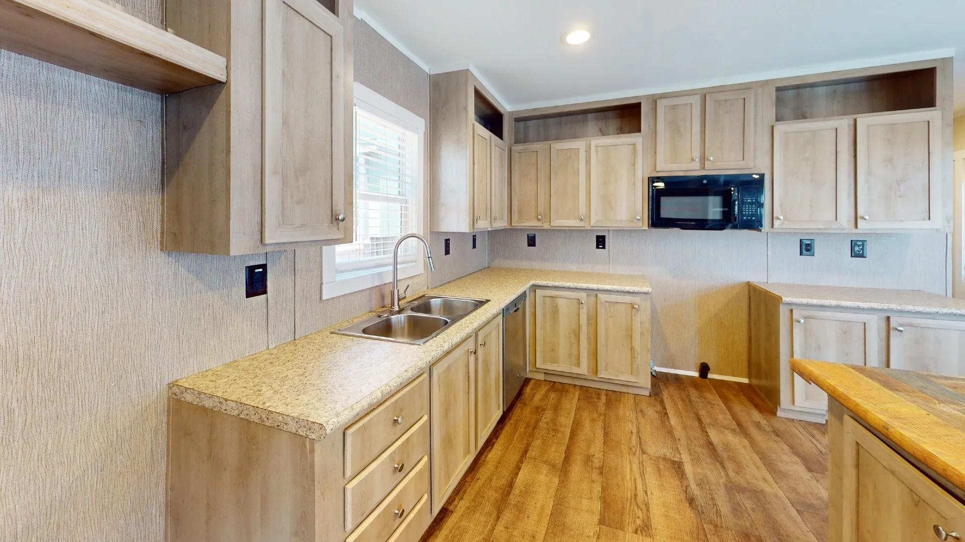 Open-concept kitchen featuring wood-finish flooring, light-toned cabinetry, light-colored countertops, a double basin sink with a high-arc faucet, and an integrated microwave