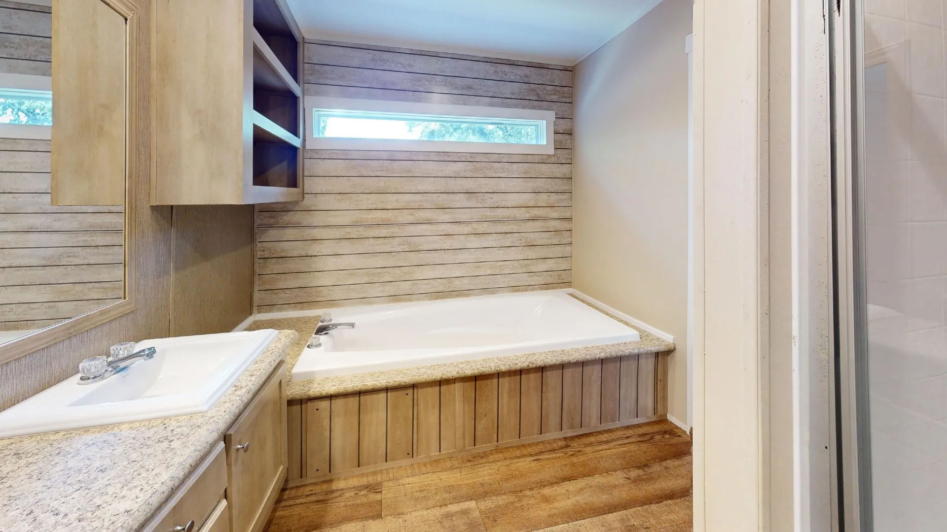 Bathroom featuring a built-in soaking tub with wood-finish paneling, a vanity with a white basin sink and light-colored countertop, and a mirrored wall