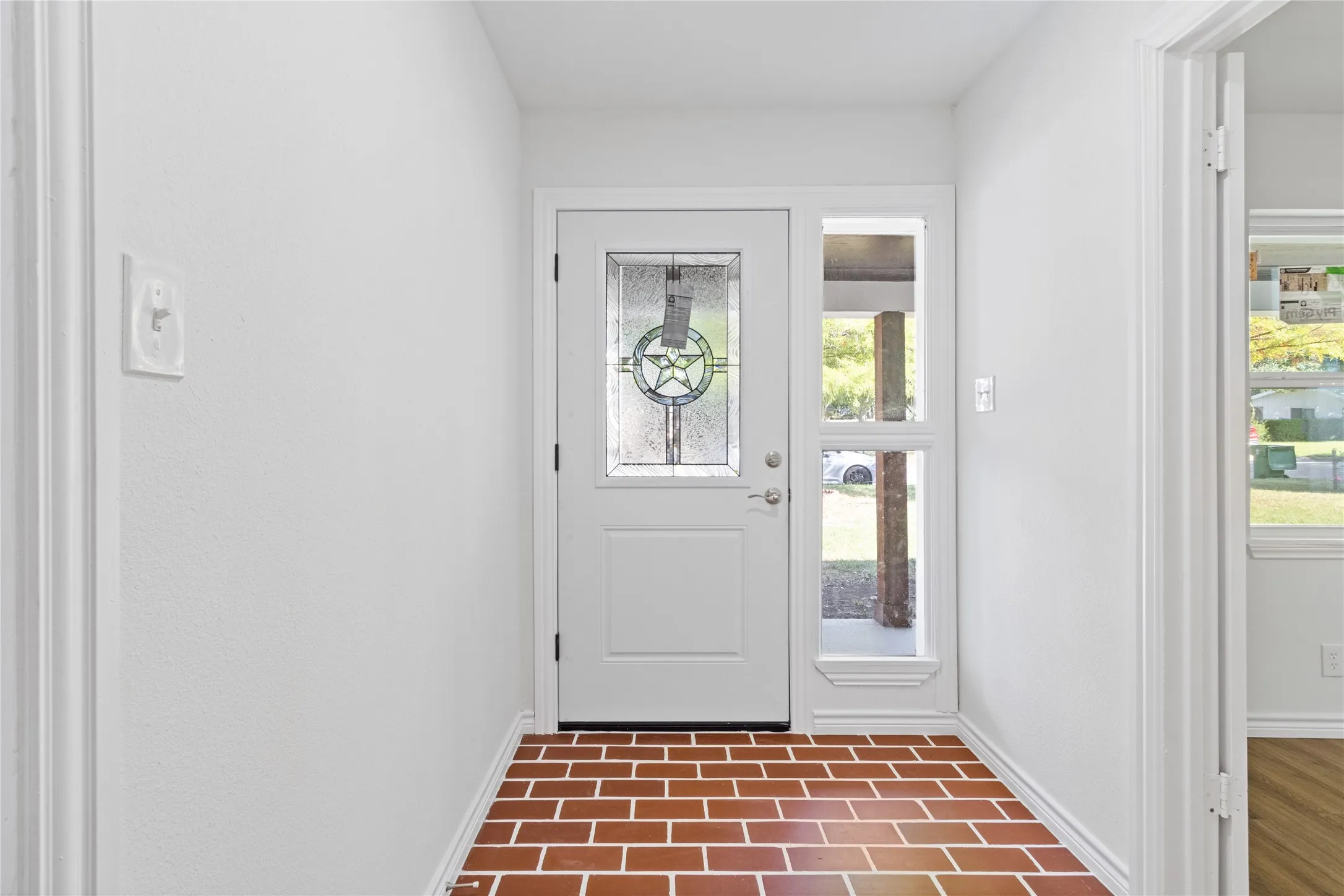 Foyer featuring brick-pattern tile flooring, a white paneled front door with decorative glass, and a matching sidelight